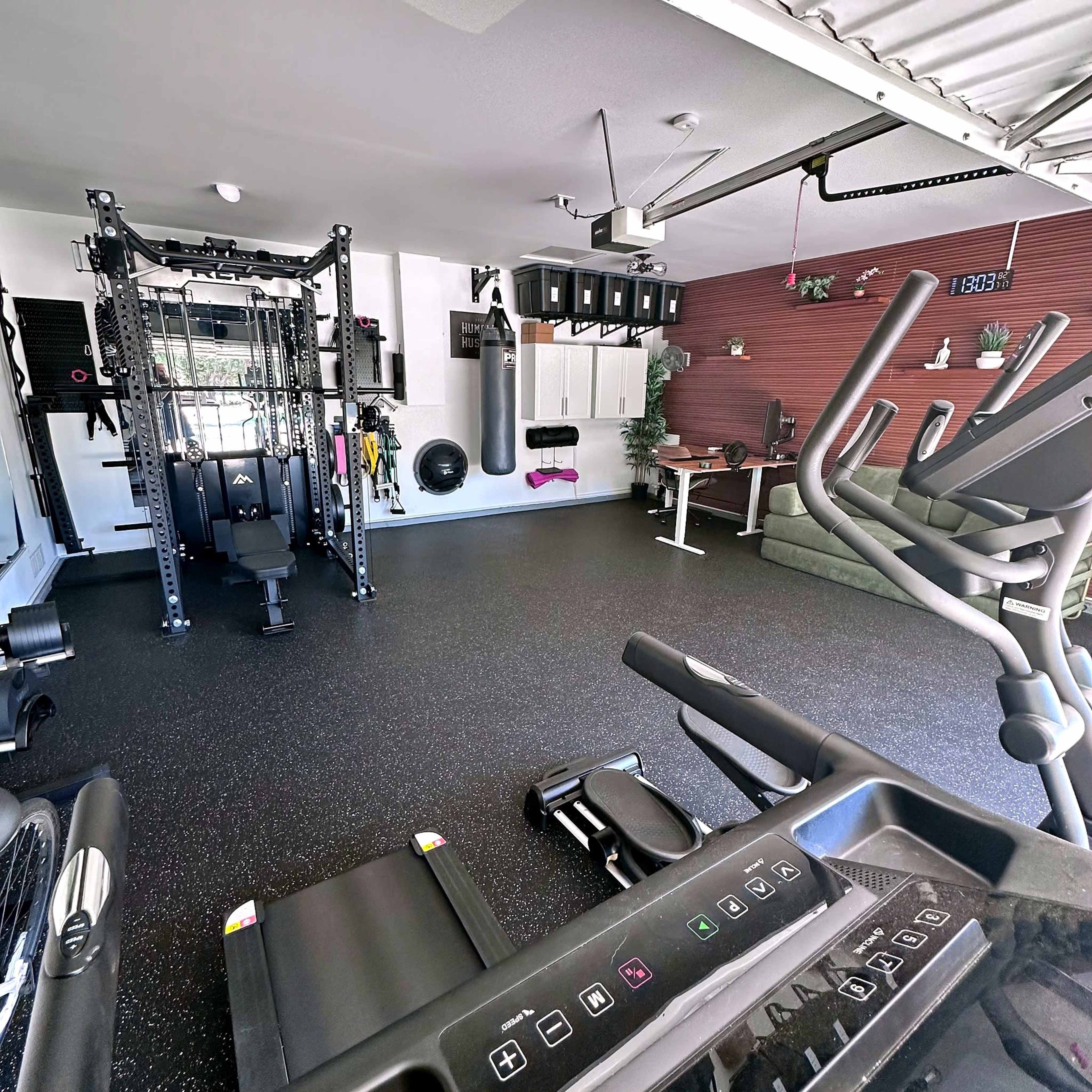 The image shows a home gym equipped with various exercise machines, a weight rack, a punching bag, and a small seating area.