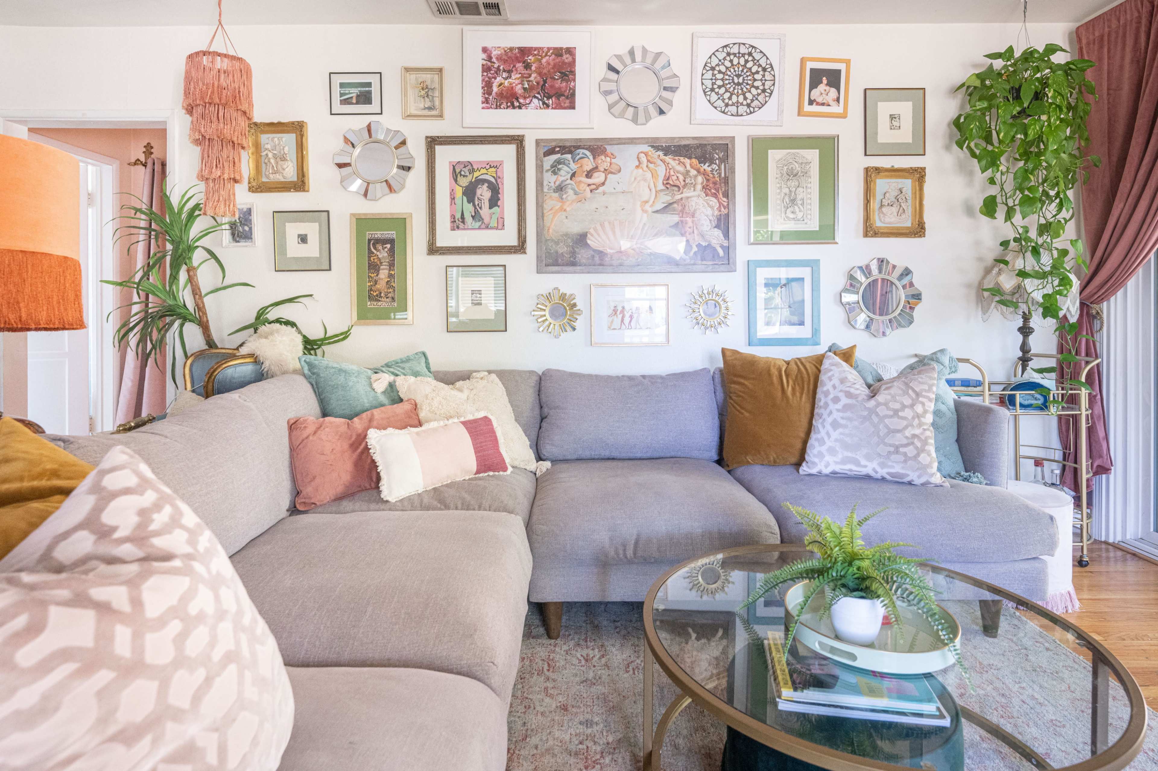 A cozy living room features a gray sectional sofa adorned with various cushions, surrounded by an eclectic gallery wall of framed art and photographs.