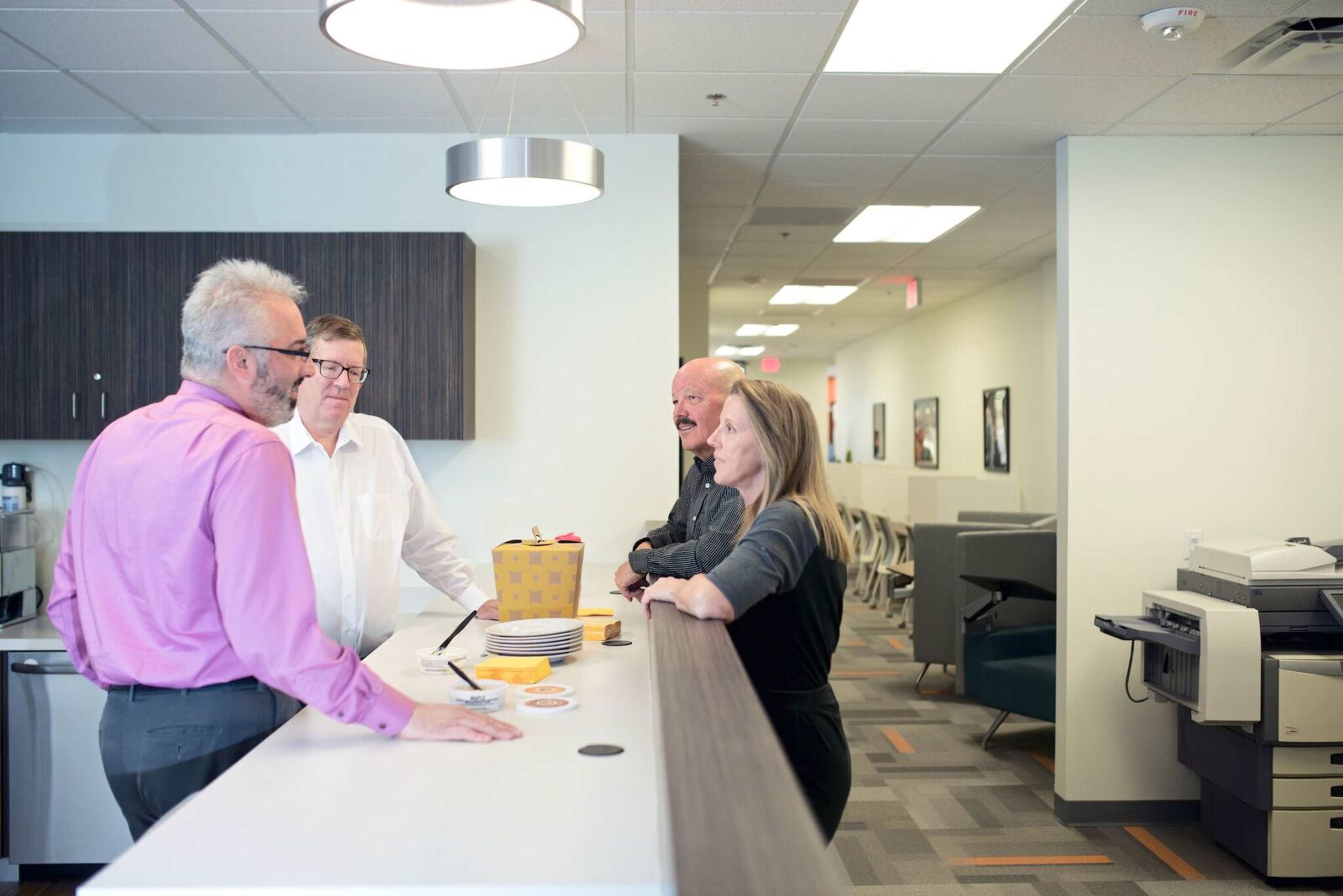 Four professionals are engaged in conversation around a counter in an office setting.