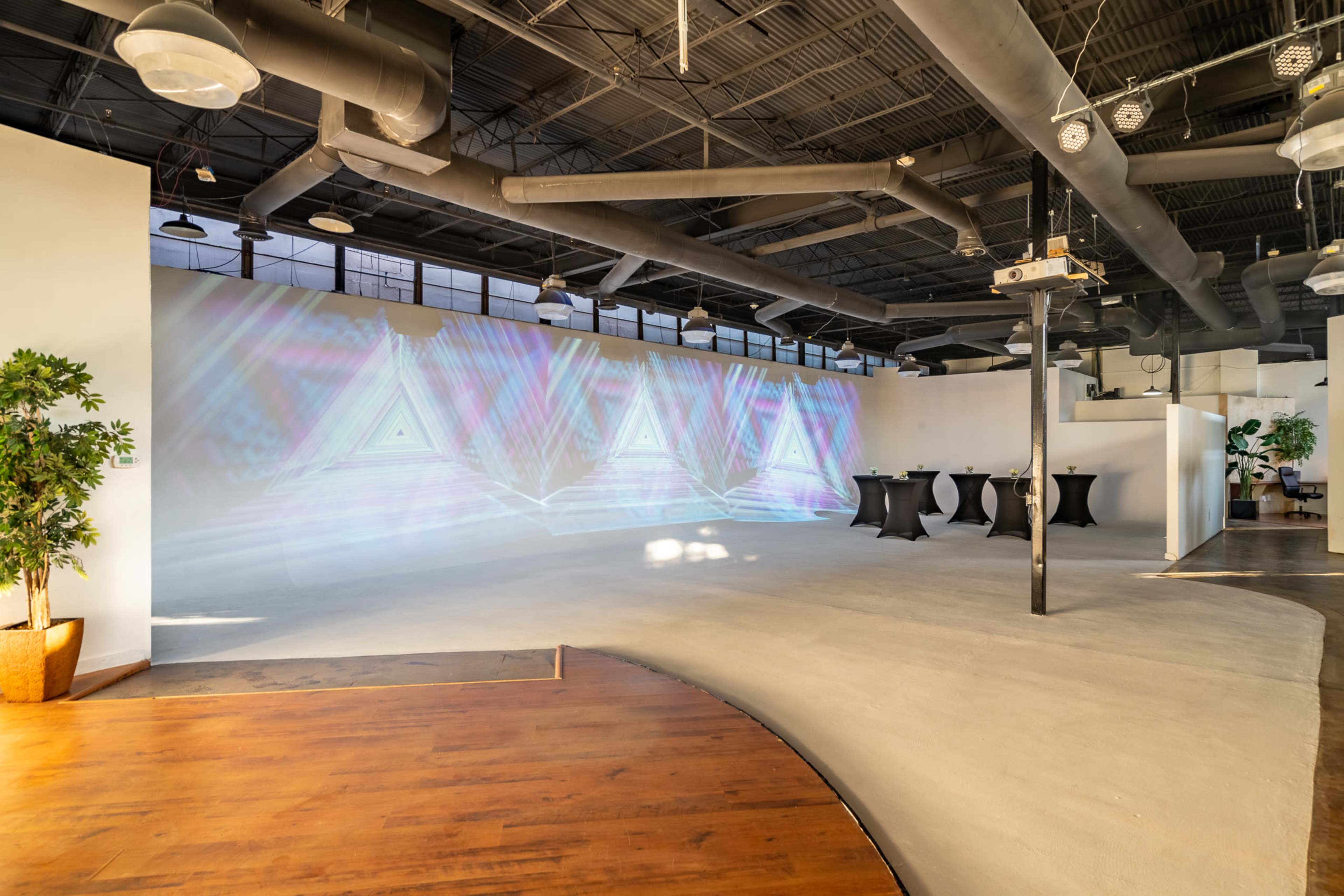 The image shows an empty event space featuring a large wall projection and several cocktail tables arranged in the area.