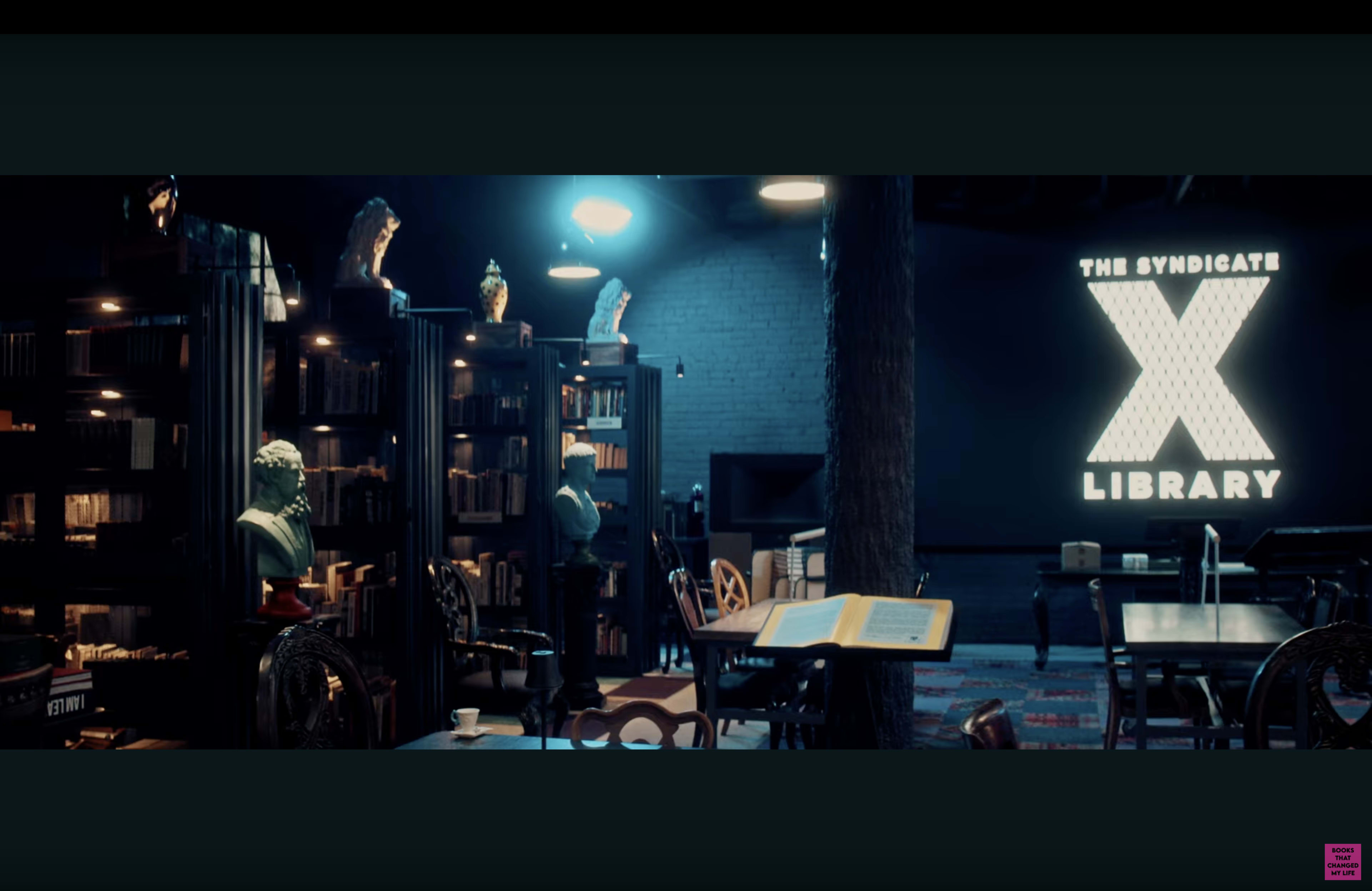 The image shows a dimly lit library with dark bookshelves, a large illuminated sign reading "THE SYNDICATE X LIBRARY," and various sculptures displayed on top of the shelves.