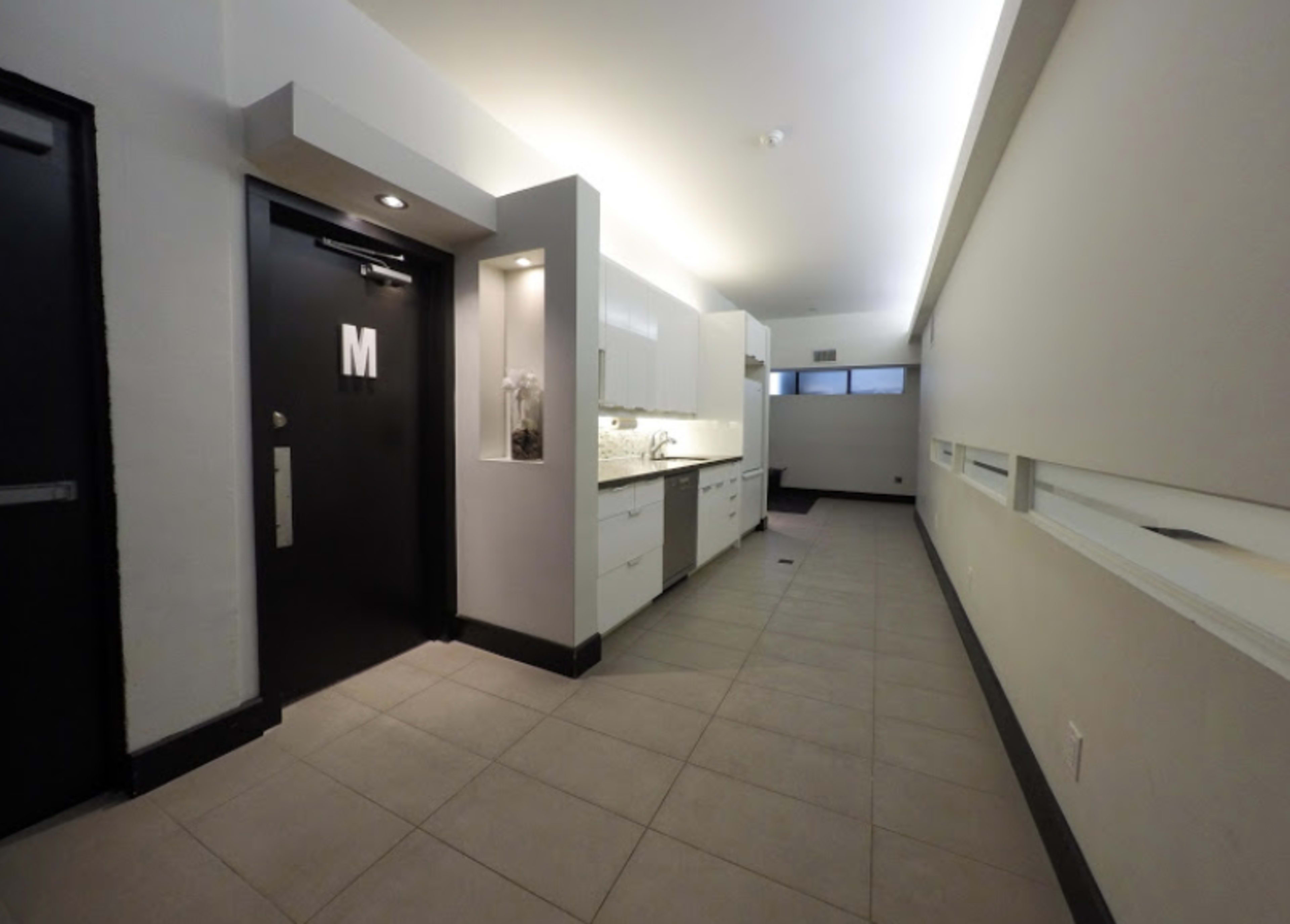 The image features a modern hallway with a kitchenette on the left and a door labeled "M" at the end.
