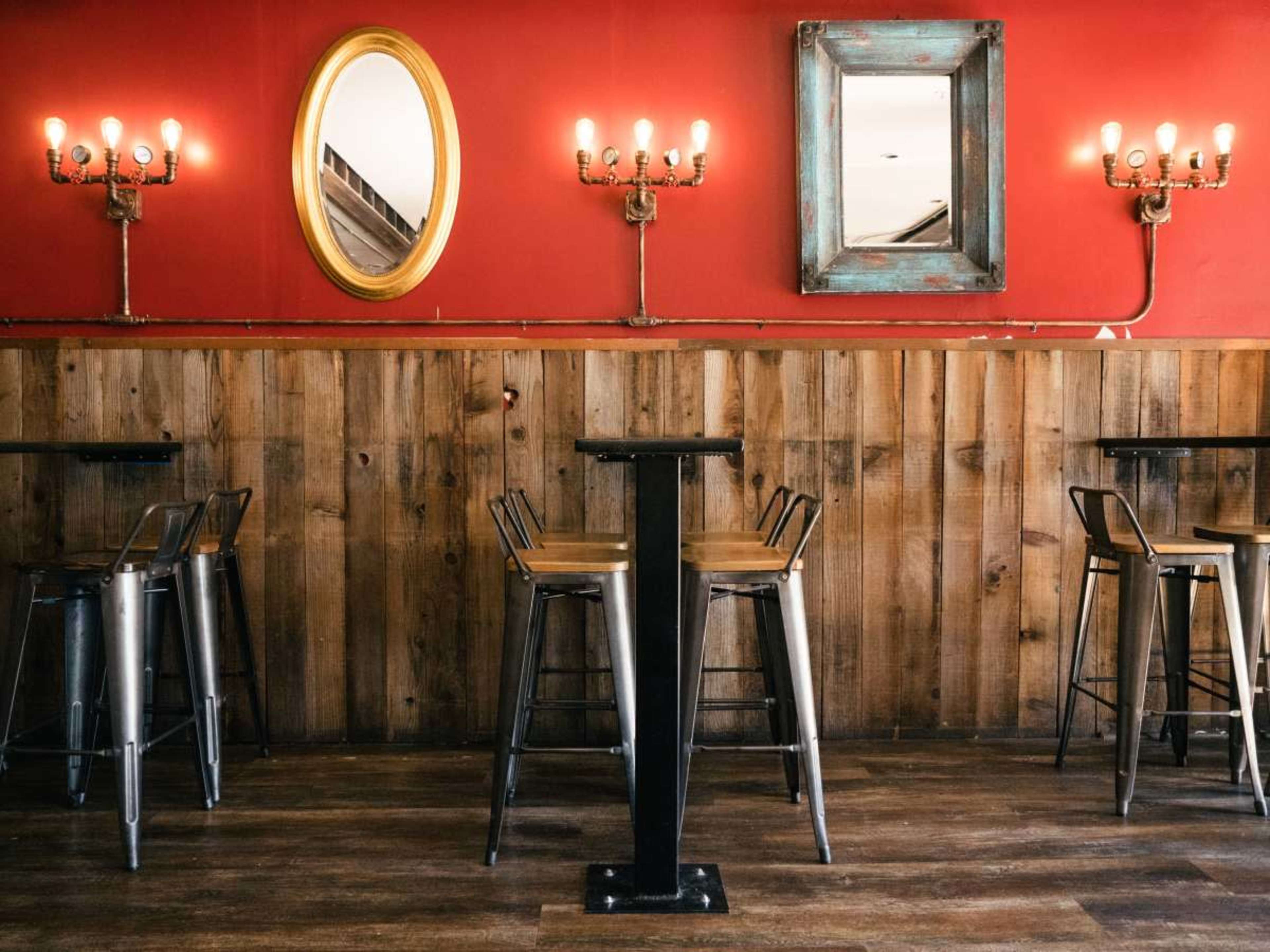 The image shows a rustic restaurant interior with wooden walls, metal bar stools, and two mirrors above a low wooden partition, all highlighted by warm lighting.