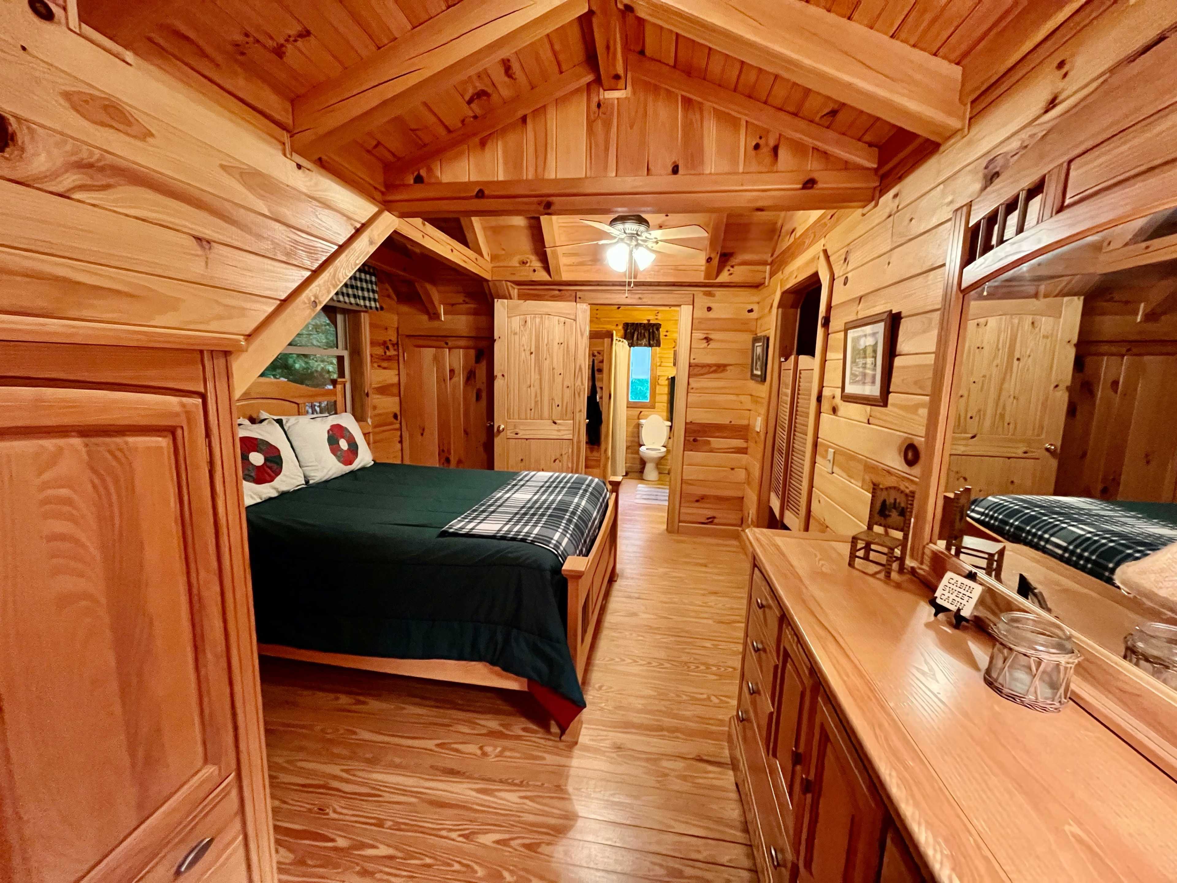 A wooden-paneled cabin interior featuring a bedroom with a bed, dresser, and an adjoining bathroom area.