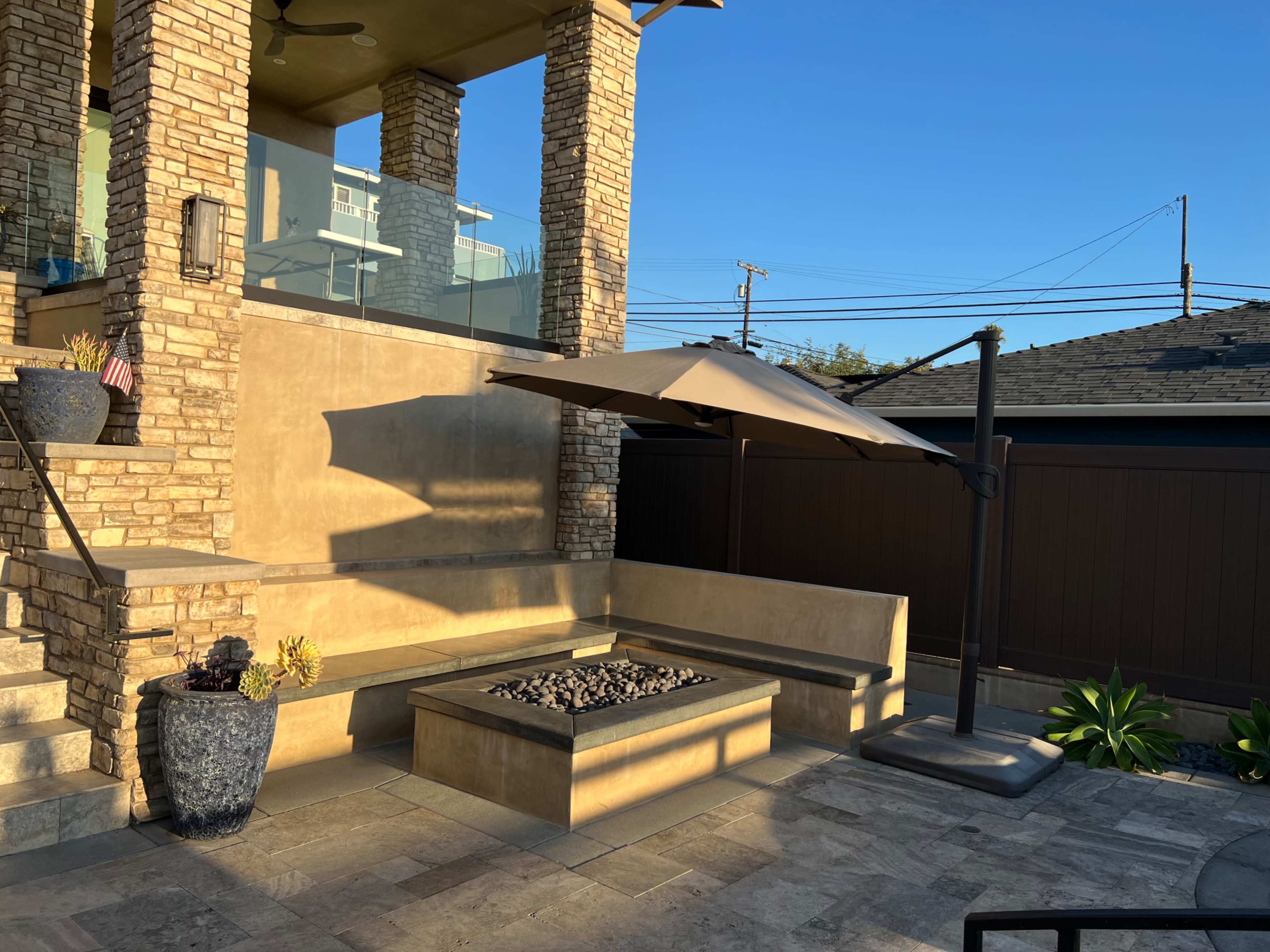 A patio area featuring a stone fire pit, a large umbrella, and a seating arrangement made of concrete.