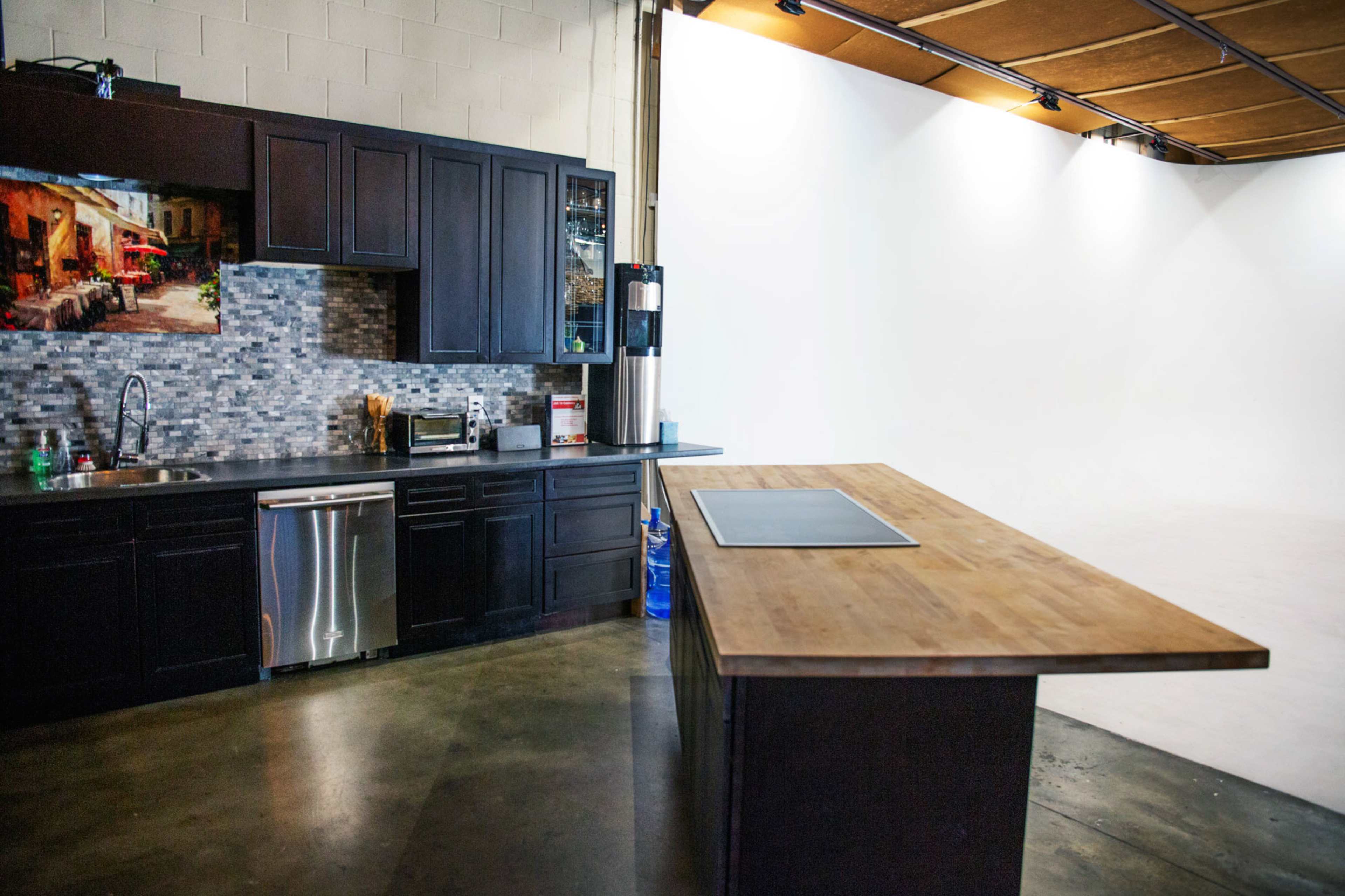 A modern kitchen features dark cabinetry, a mosaic backsplash, stainless steel appliances, and a wooden island in a spacious, brightly lit area.