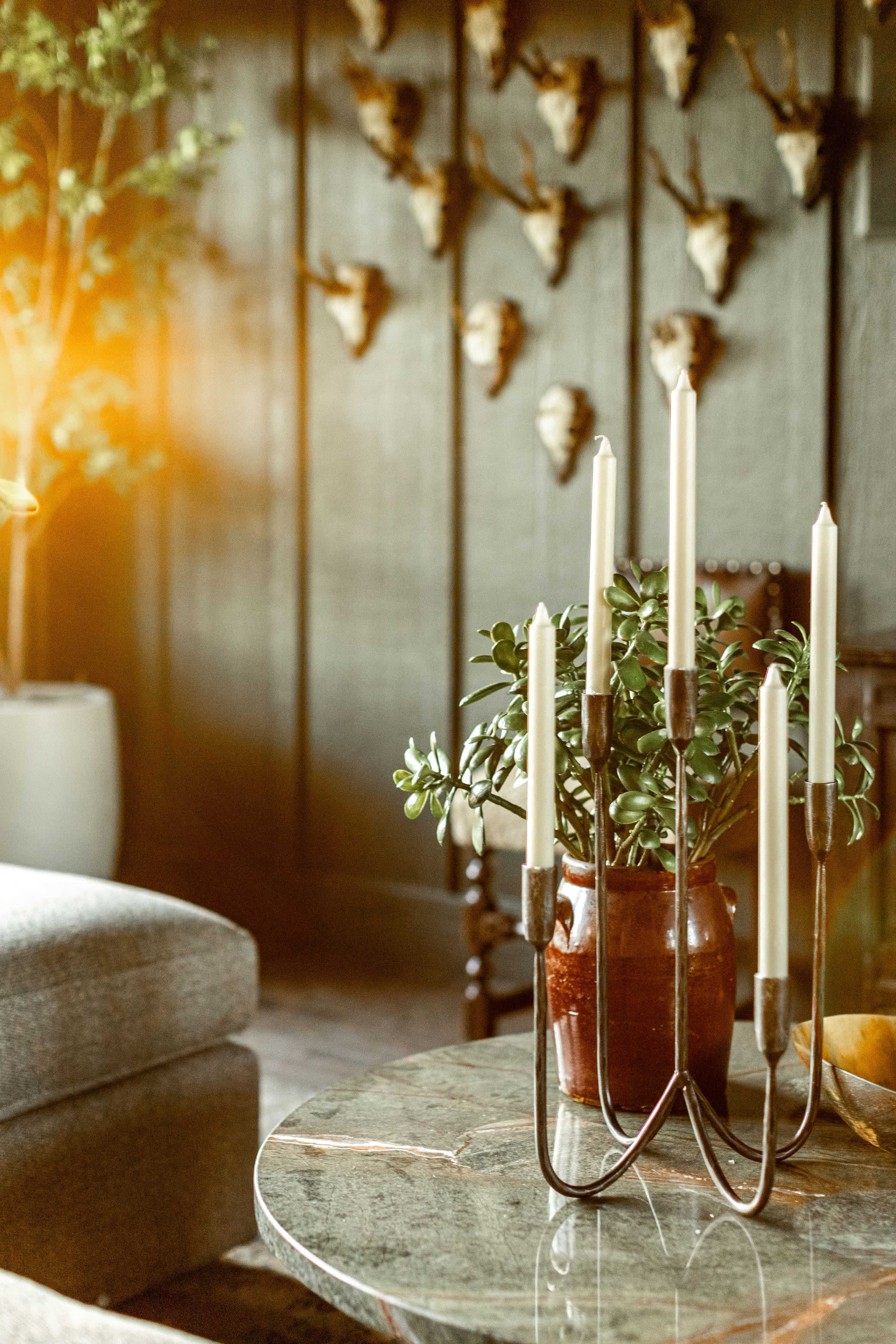 A candle holder with five candles stands on a marble table in a room featuring a wall adorned with mounted animal heads.