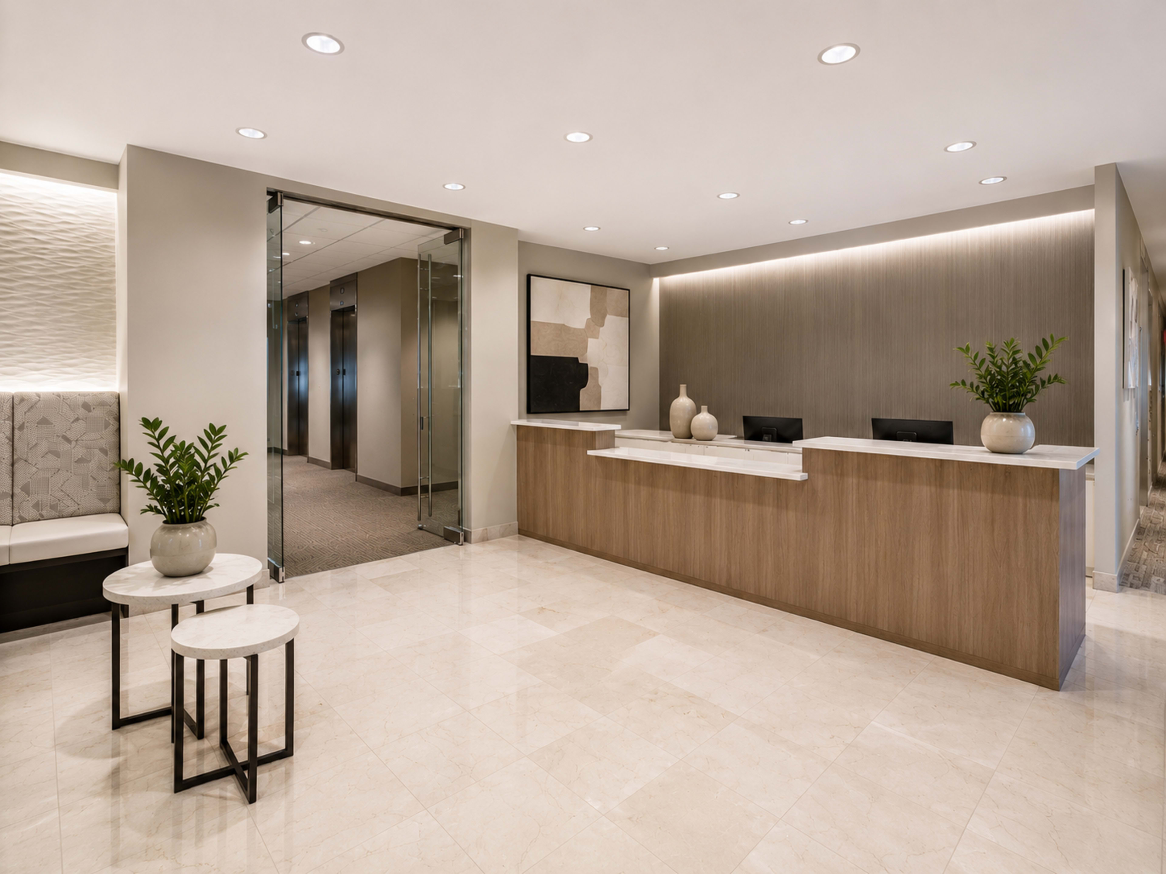 The image shows a modern reception area with a wooden front desk, elegant seating, and small decorative tables, featuring plants and artwork on the walls.