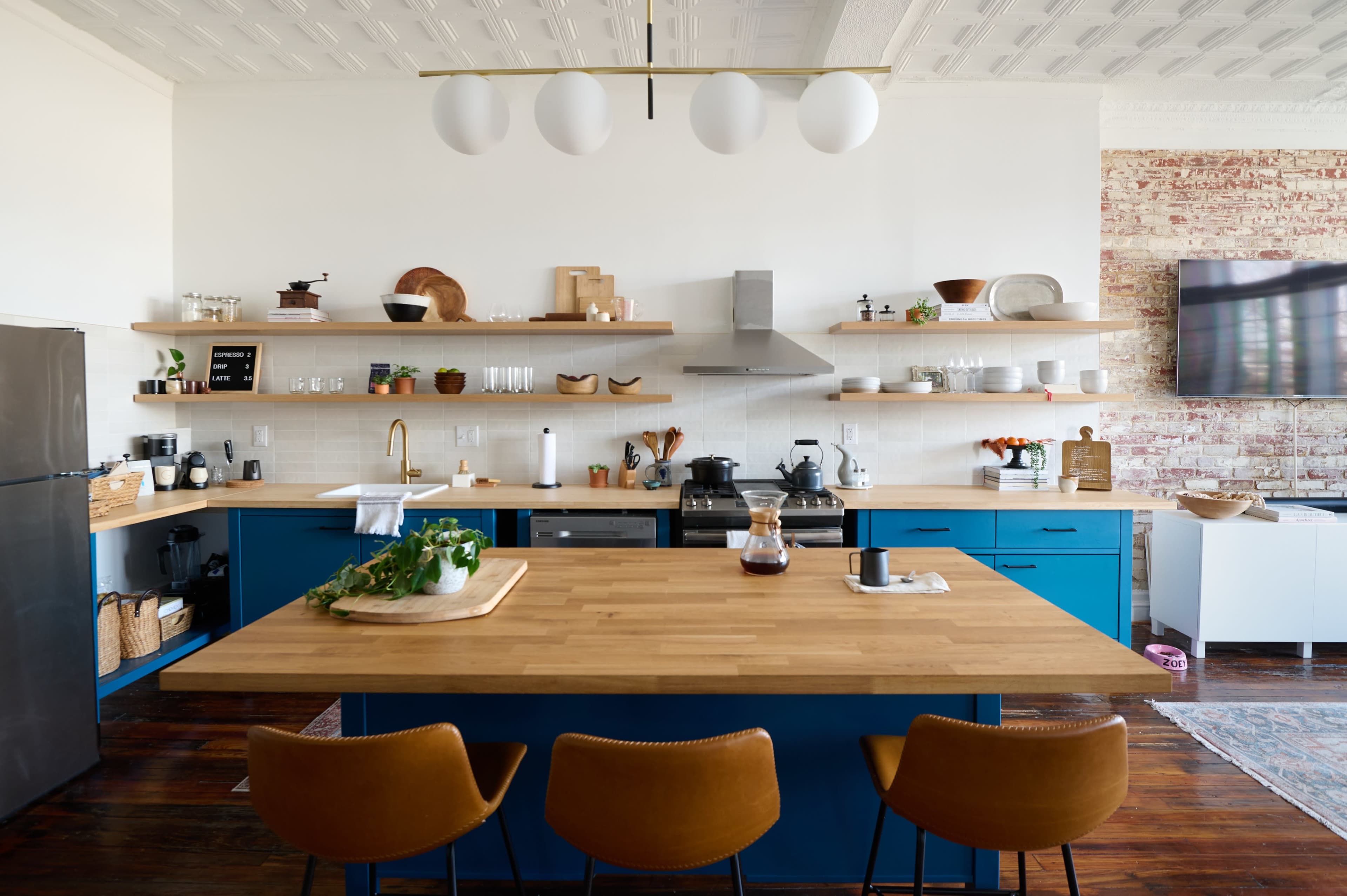 A modern kitchen features blue cabinetry, a large wooden island, and open shelving displaying various kitchenware.