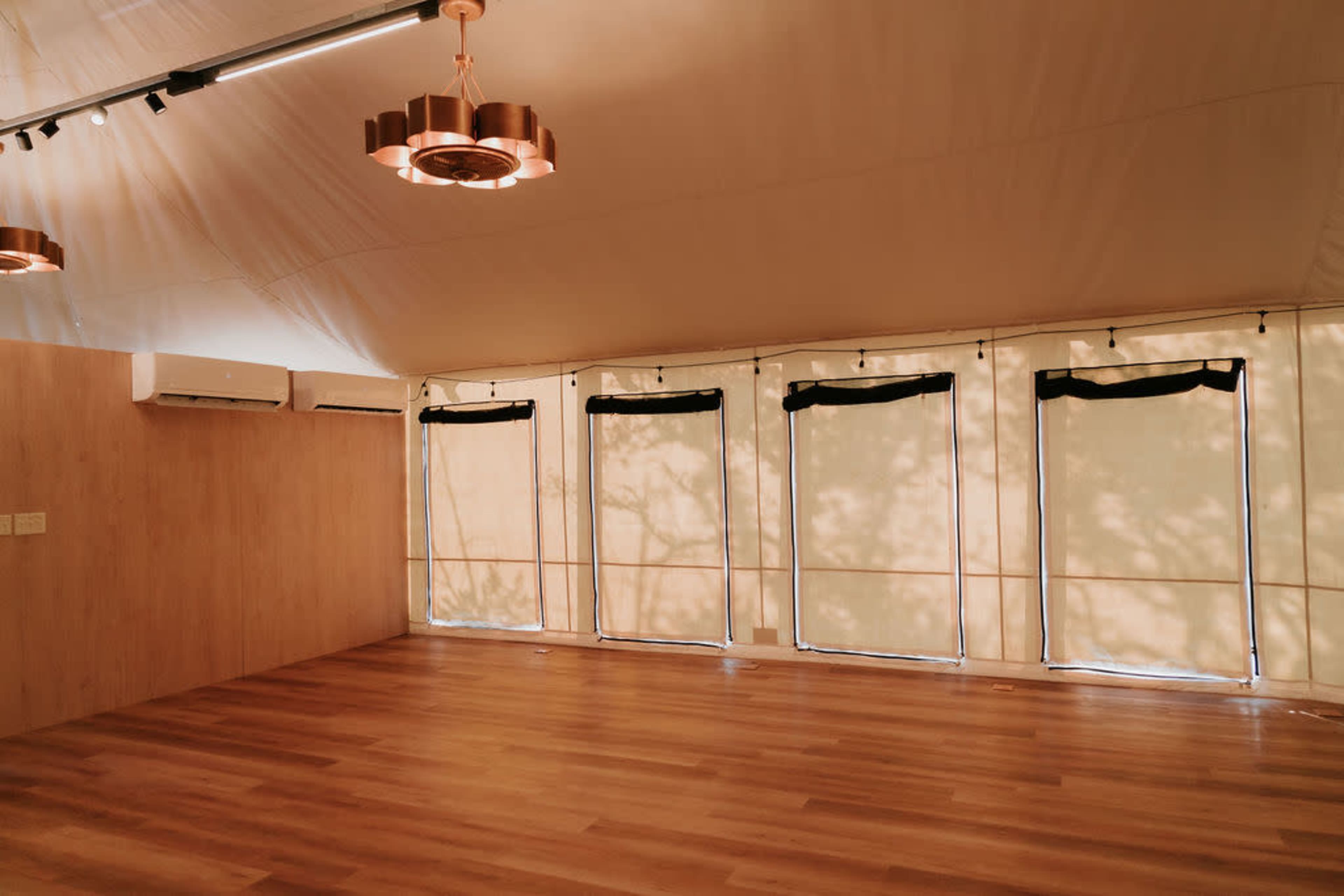 The interior features a spacious area with wooden flooring and several large windows covered by light-colored curtains.