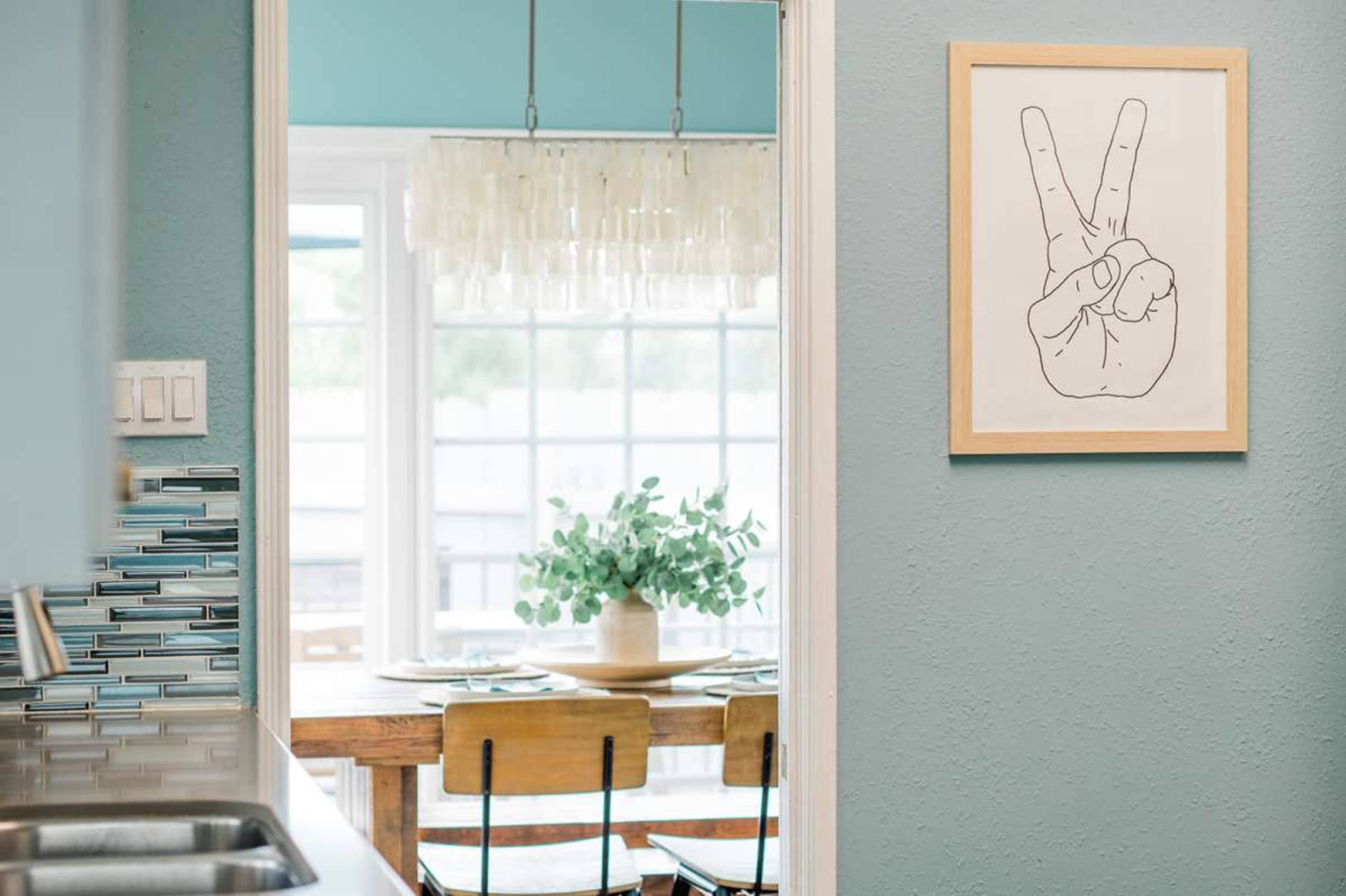 A hand-drawn peace sign is framed on a wall, leading to a dining area with a wooden table and light blue walls.