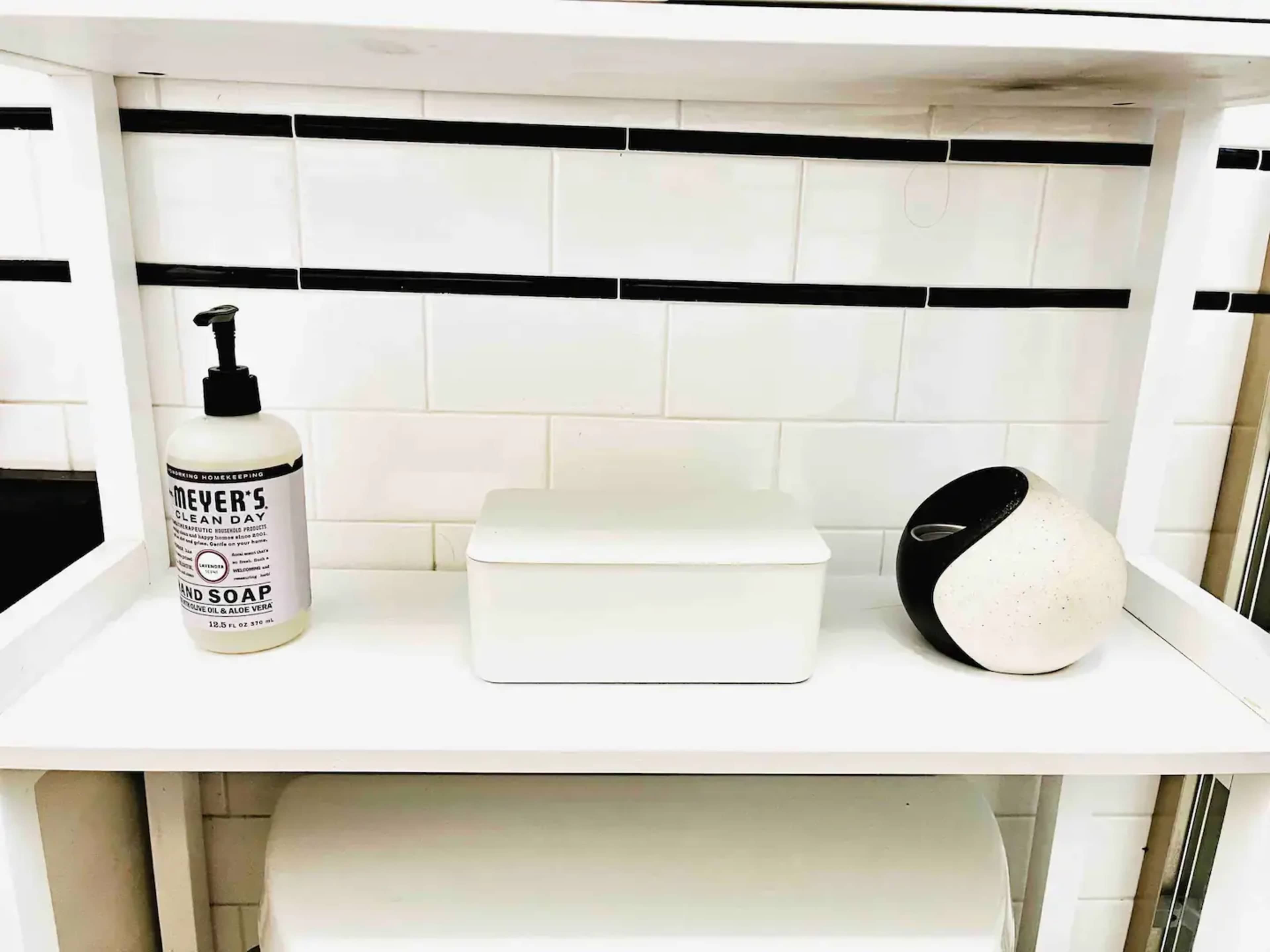 A white shelf displays a bottle of soap and a small, decorative container beside a white box.