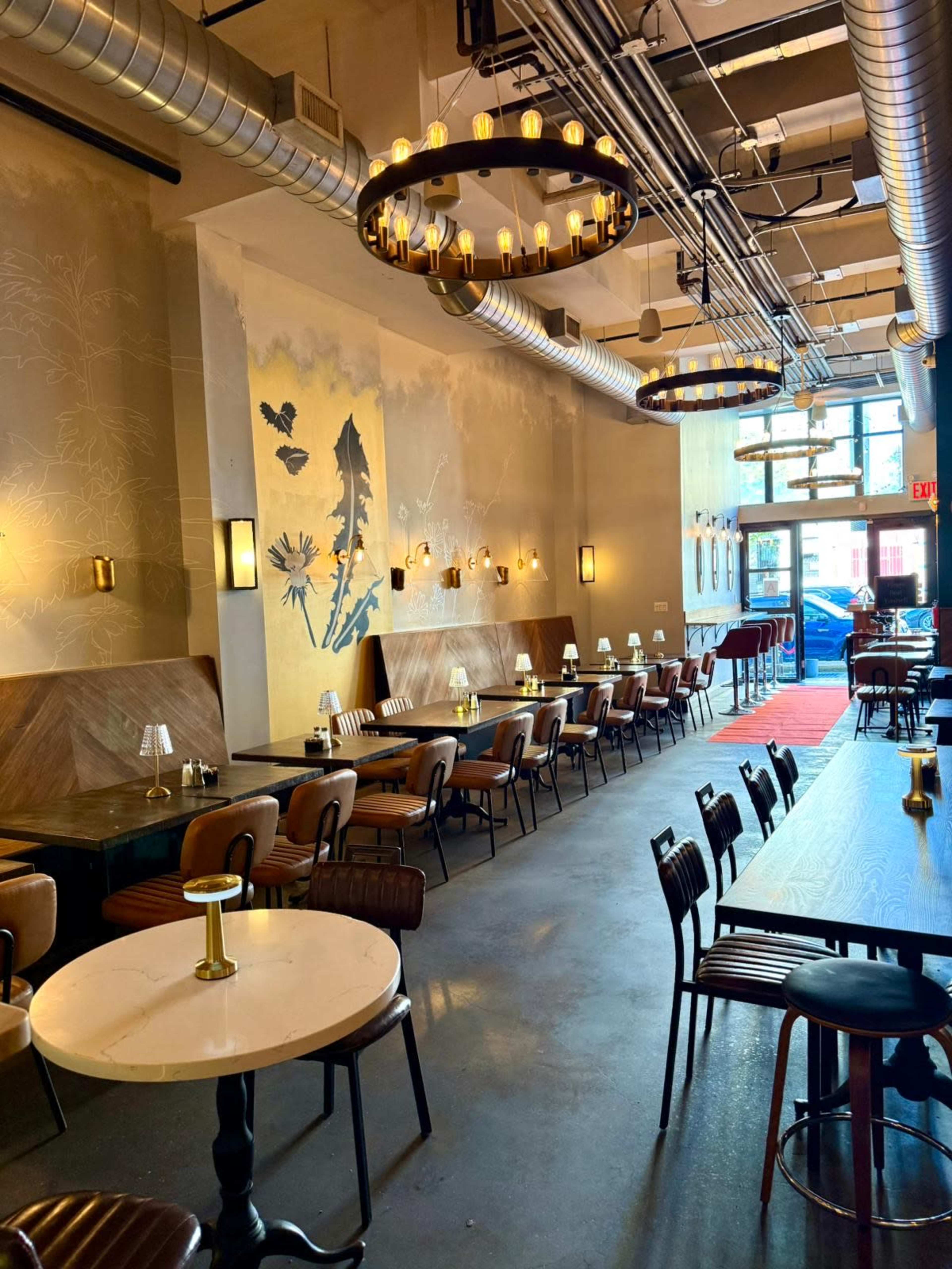 The image shows an interior of a modern restaurant featuring rows of tables with chairs, decorative lighting, and wall art.