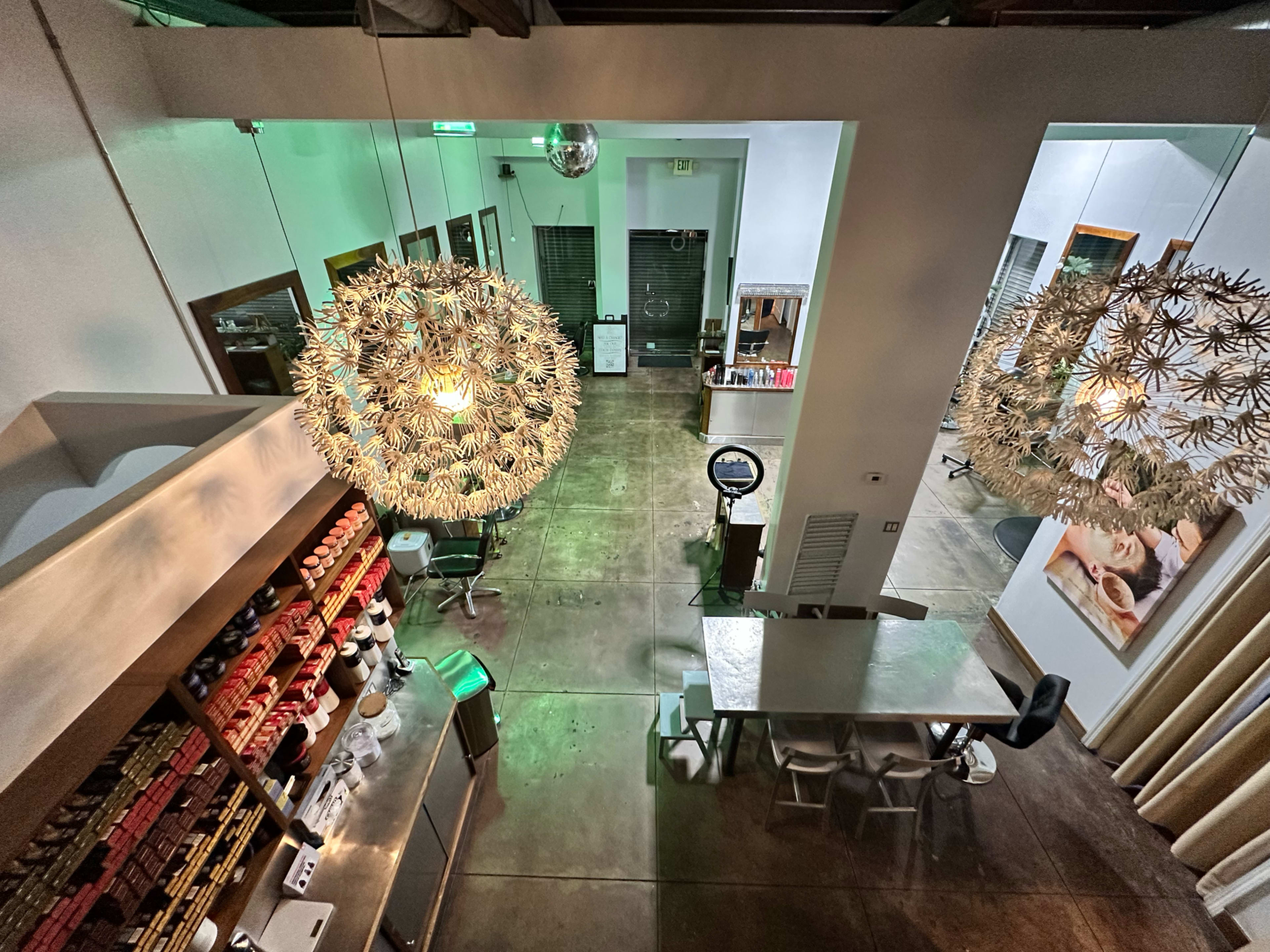 The interior of a modern space features two large decorative chandeliers, a central table with chairs, and a service counter stocked with various items.