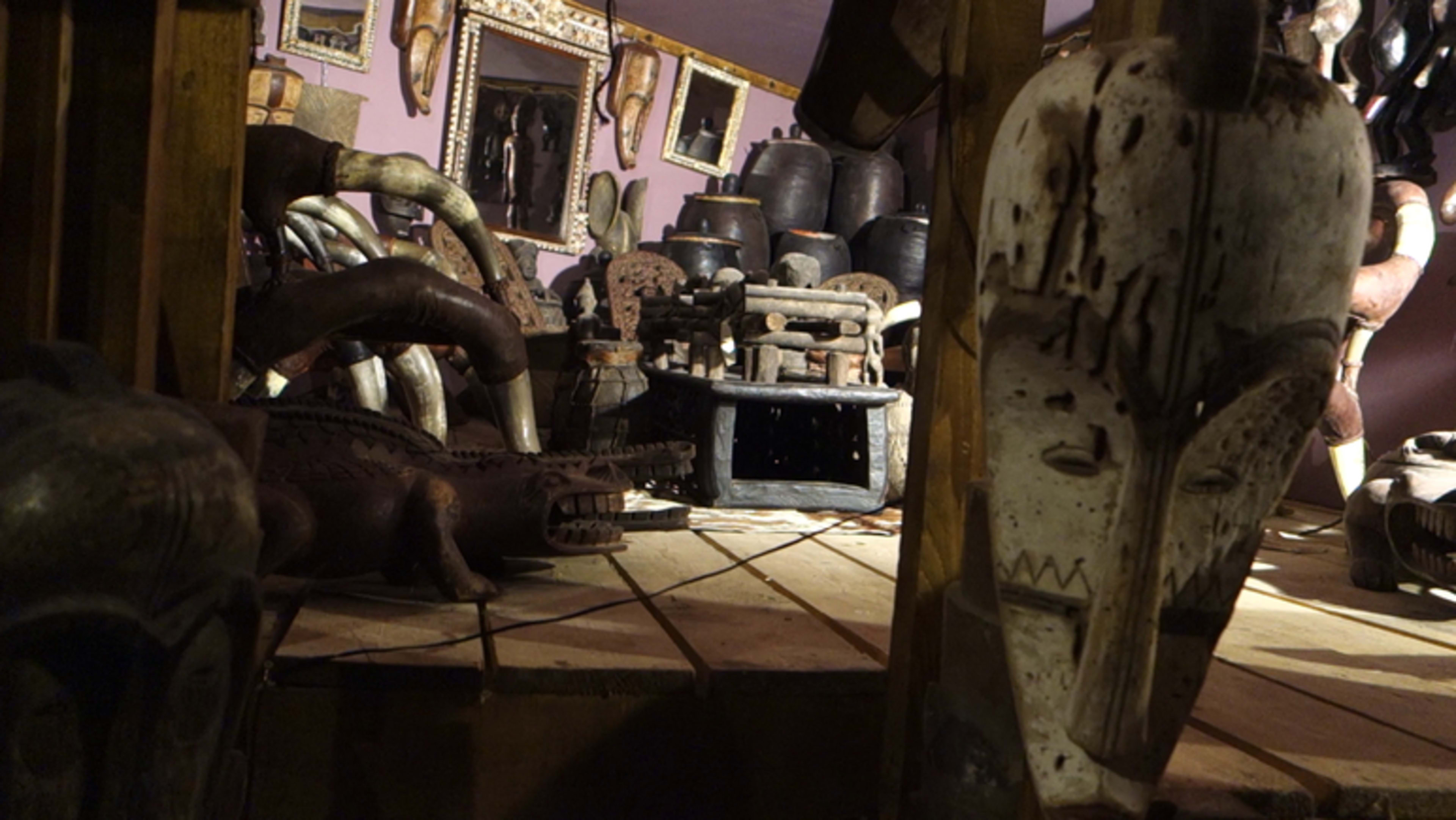 A collection of traditional wooden masks and artifacts displayed in a dimly lit gallery.