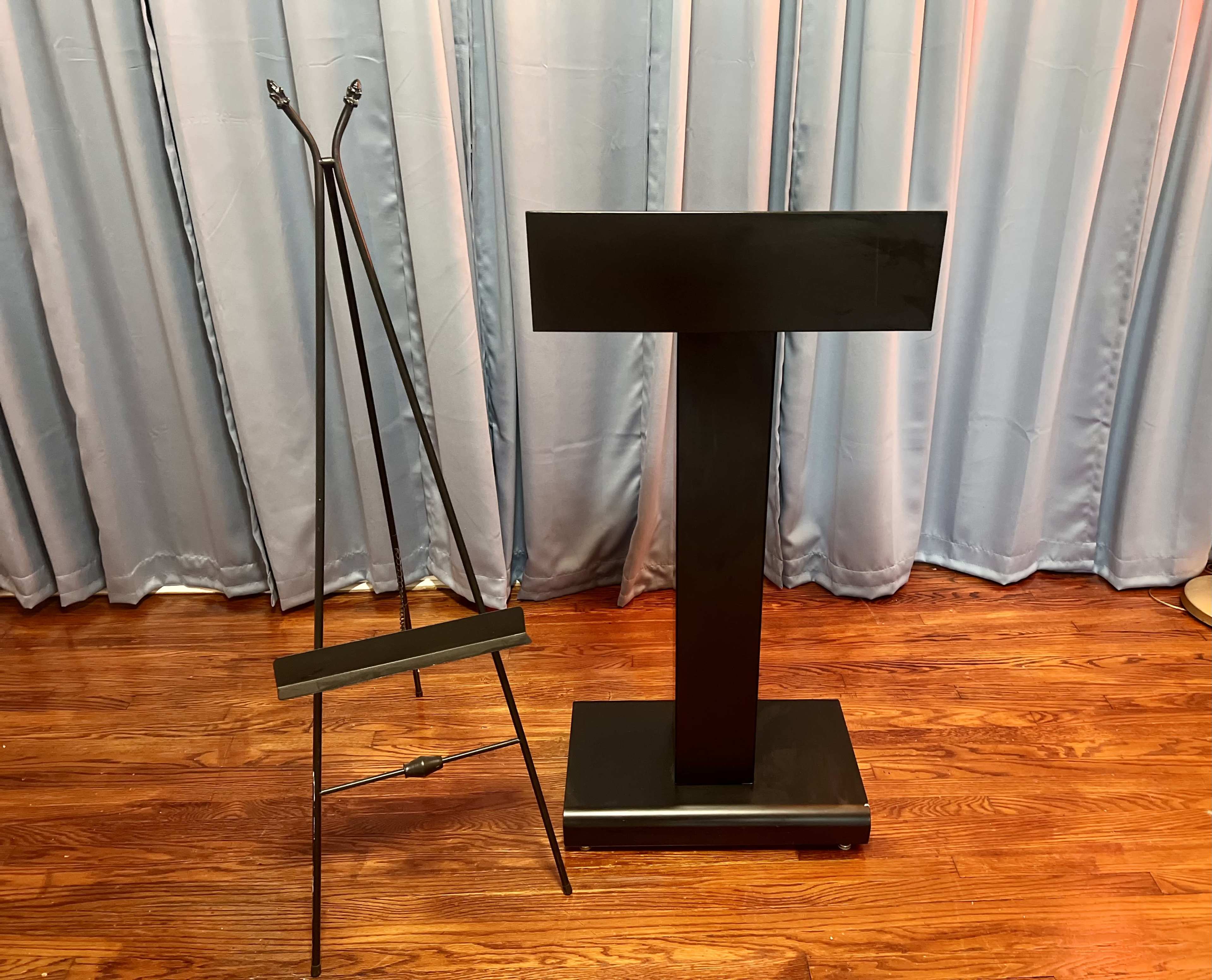A black podium stands next to a black easel against a backdrop of light blue curtains.