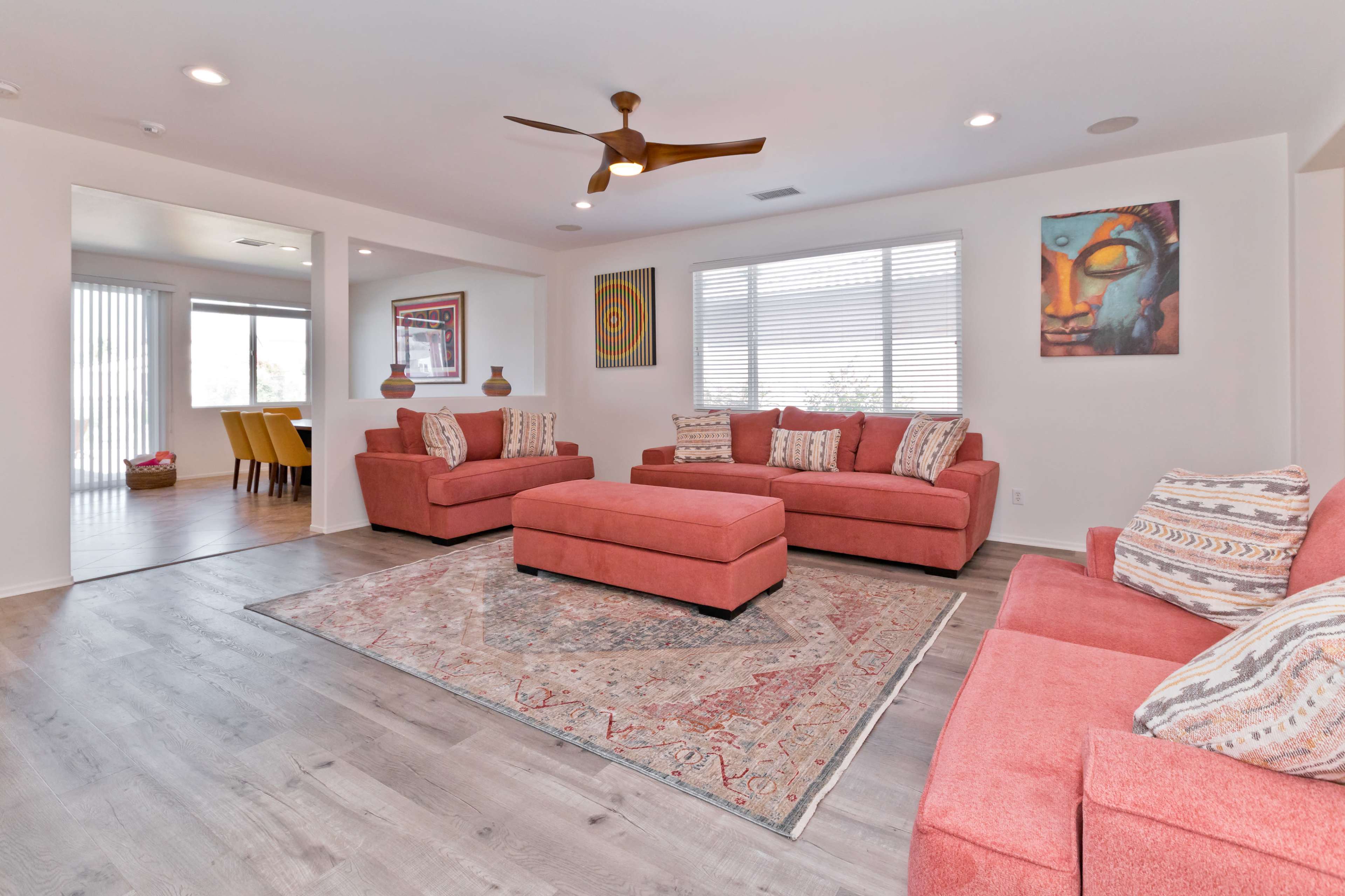 The living room features two salmon-colored sofas and an ottoman arranged around a patterned rug, with large windows providing natural light.