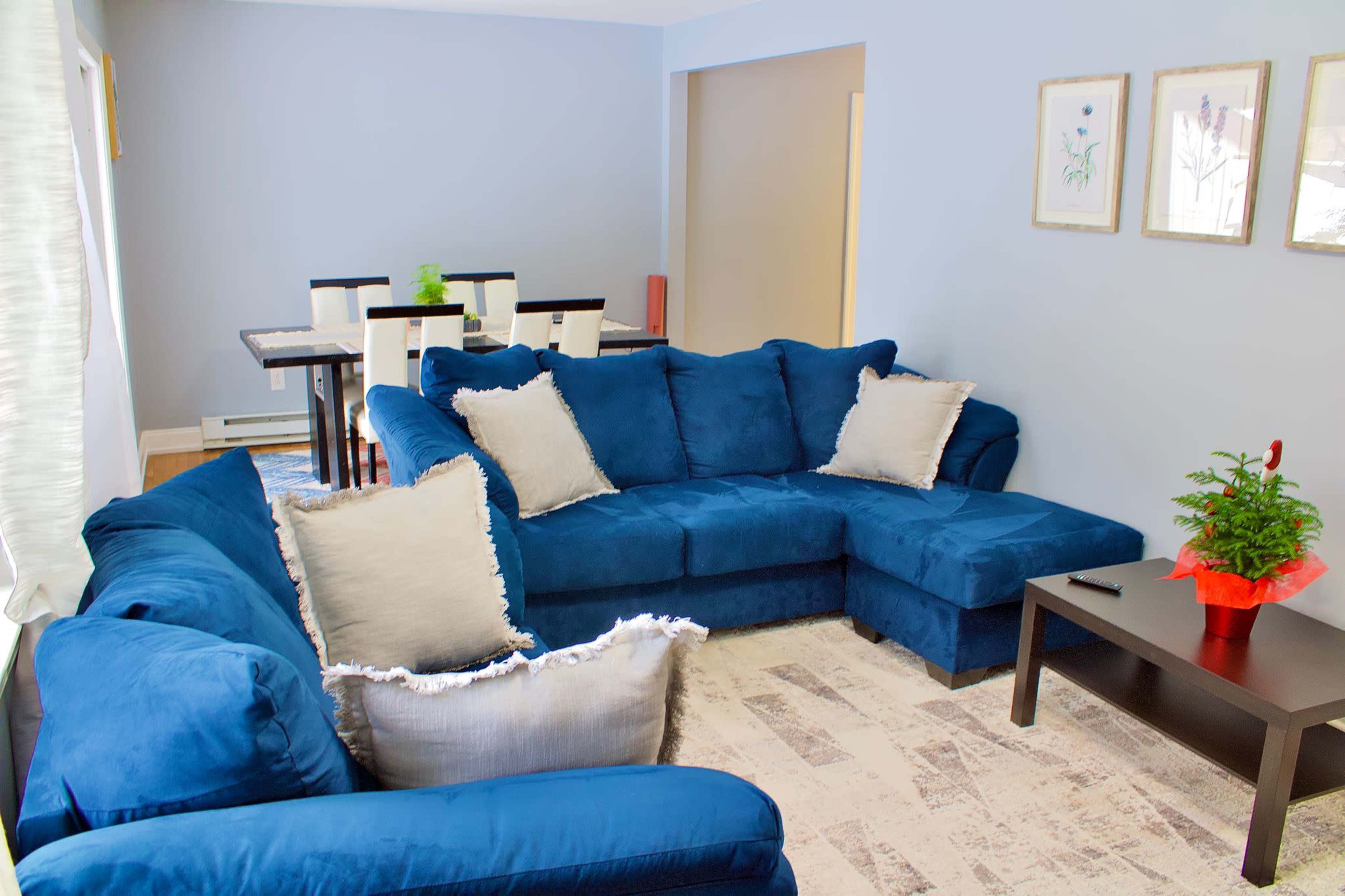 A living room featuring a blue sectional sofa, a black coffee table, and a dining area with a table and chairs in the background.