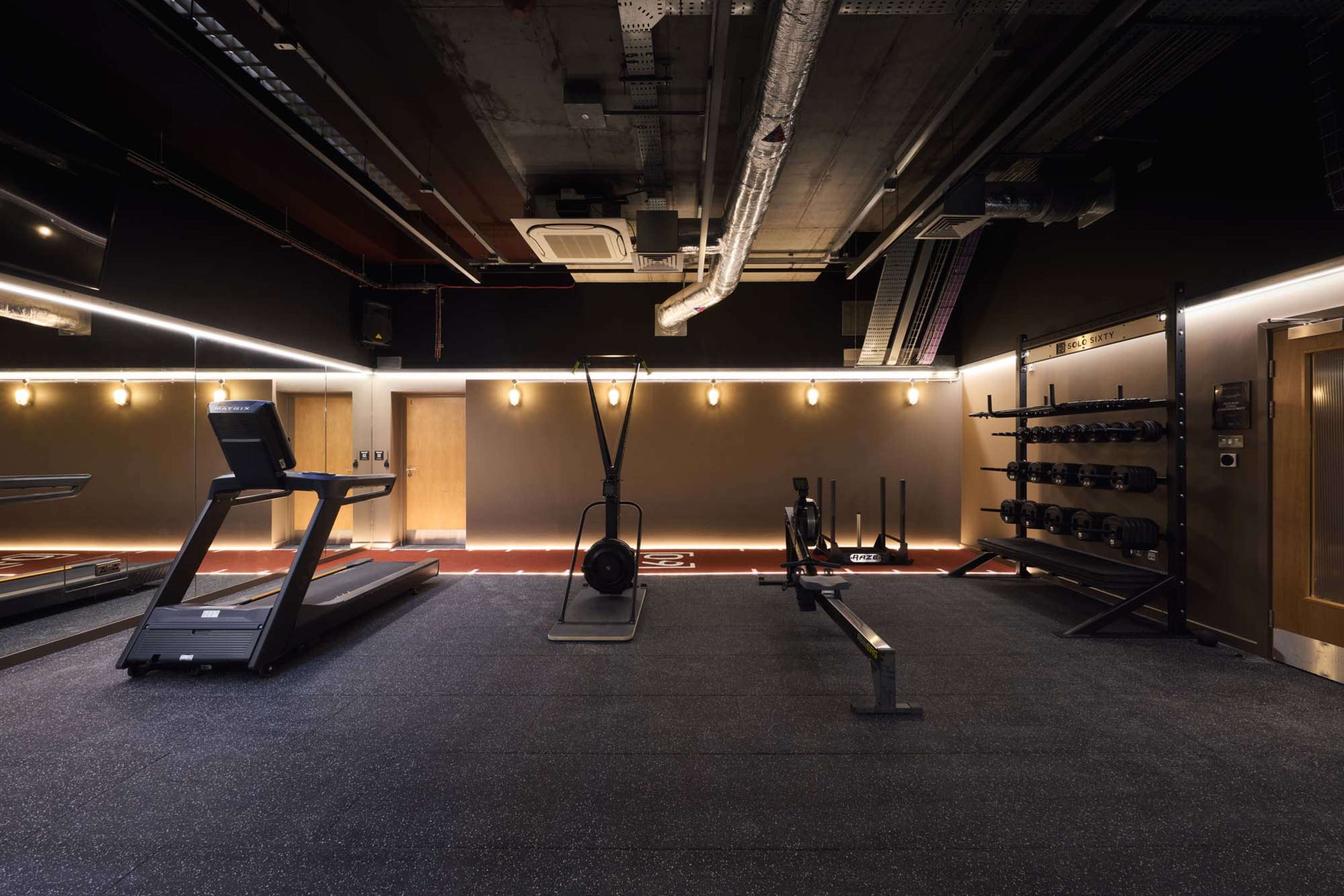 The image shows a modern gym interior equipped with various workout machines, free weights, and a rubberized floor.