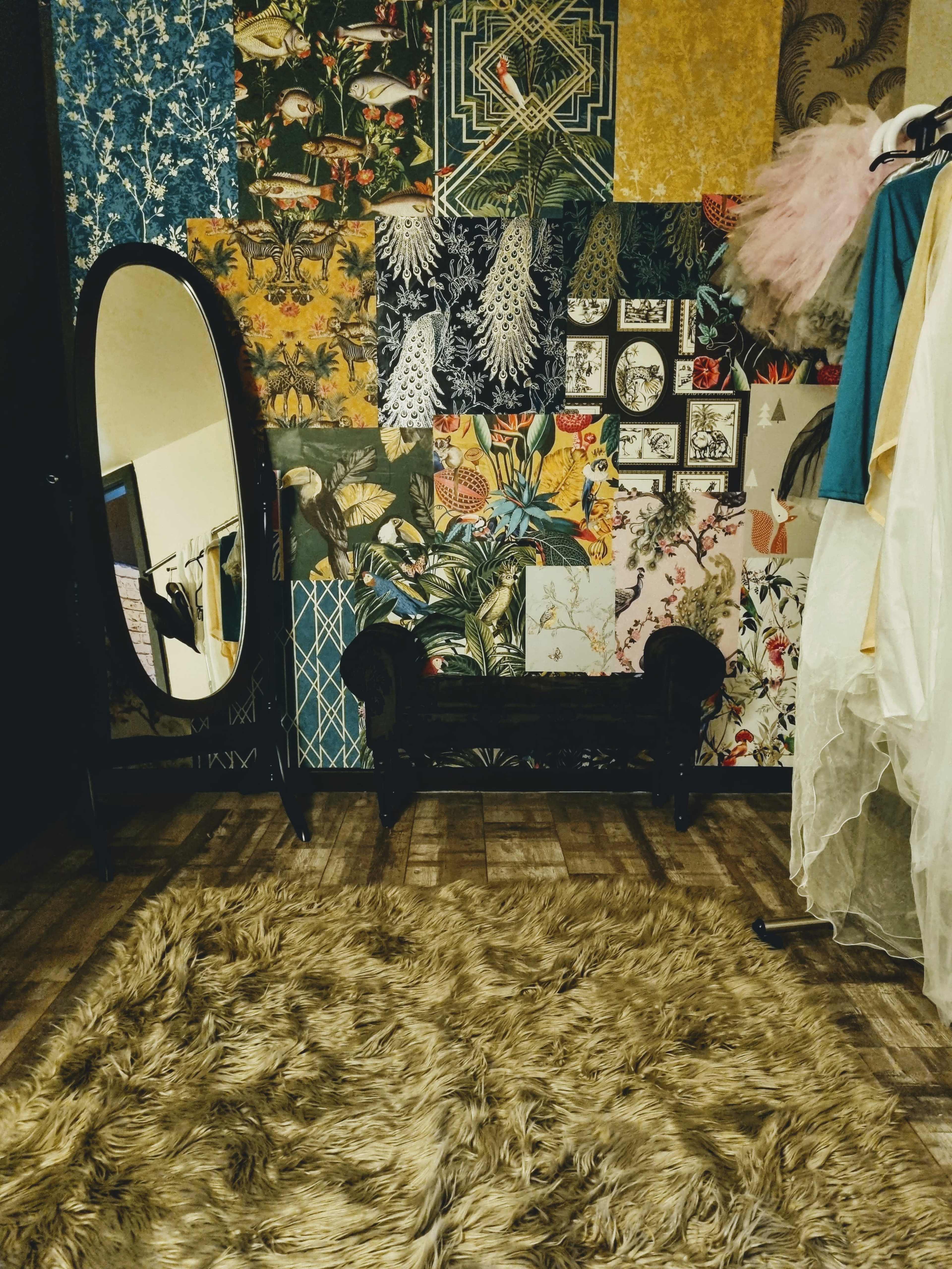 A room with a patterned wallpaper, a large oval mirror, a black bench, and a fluffy rug on the floor.
