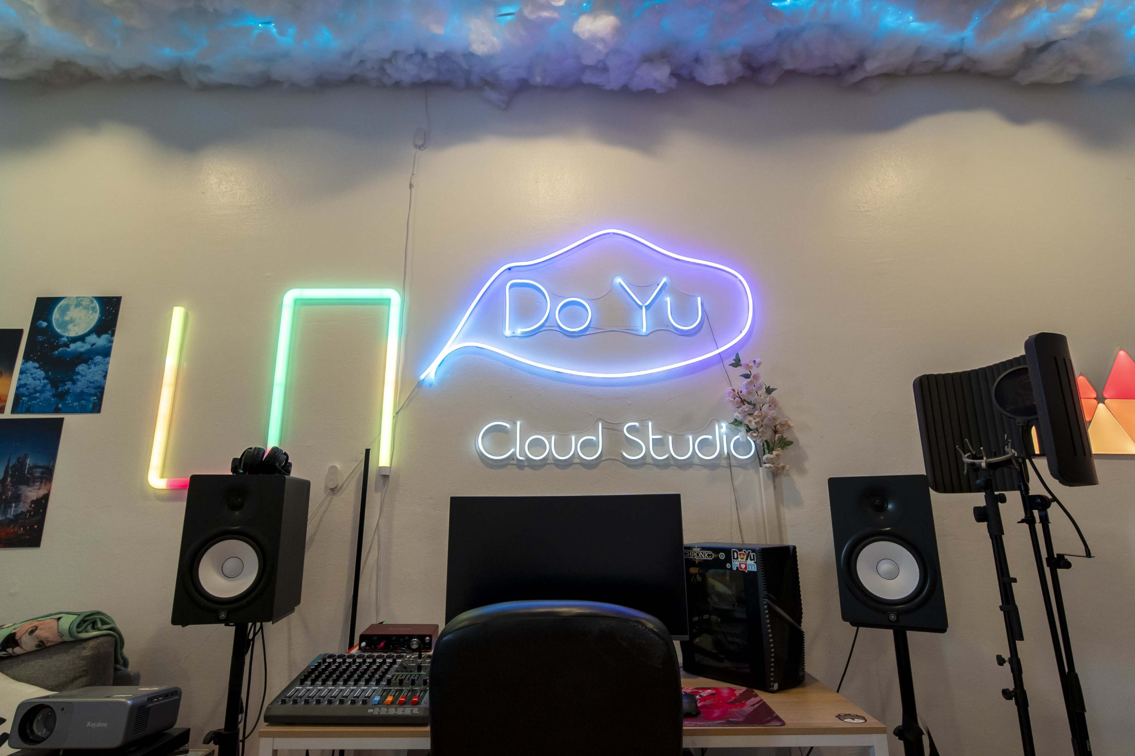 The image shows a recording studio featuring a neon sign that reads "Do Yu Cloud Studio," along with audio equipment and speakers against a white wall.