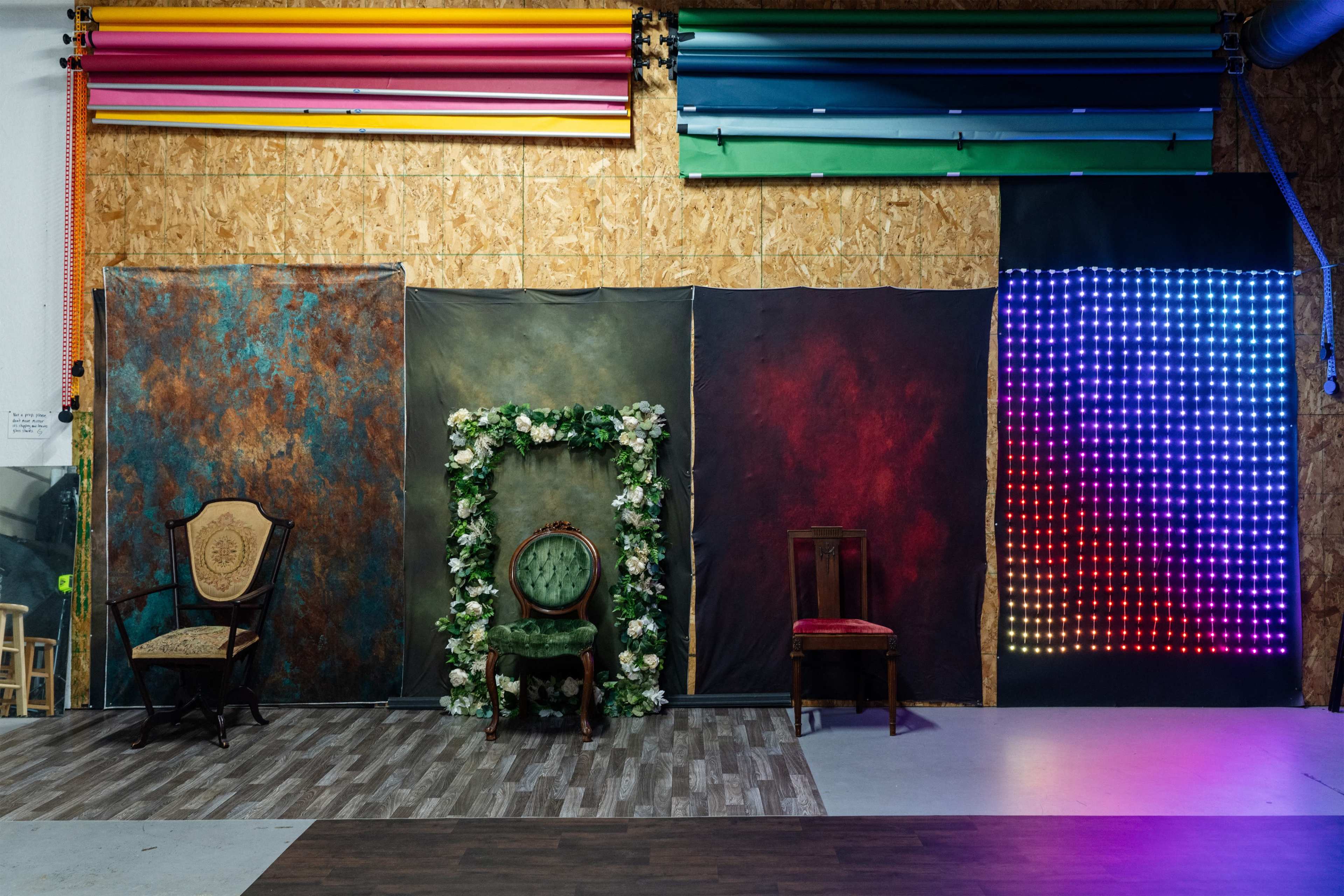 The image shows a photo backdrop setup with various textured backdrops, including a floral frame, two chairs, and a colorful LED panel.
