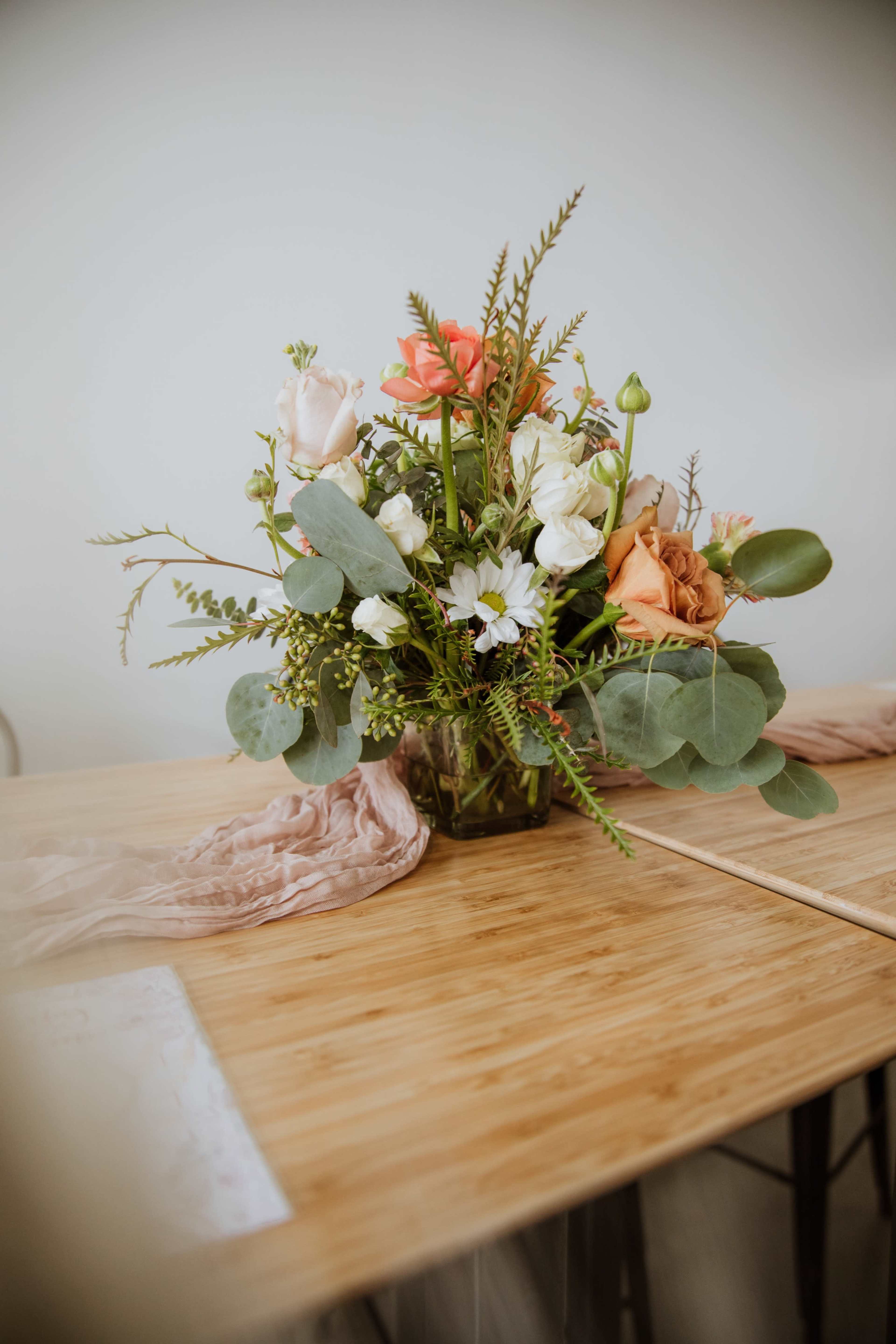 A colorful floral arrangement in a glass vase is displayed on a wooden table.