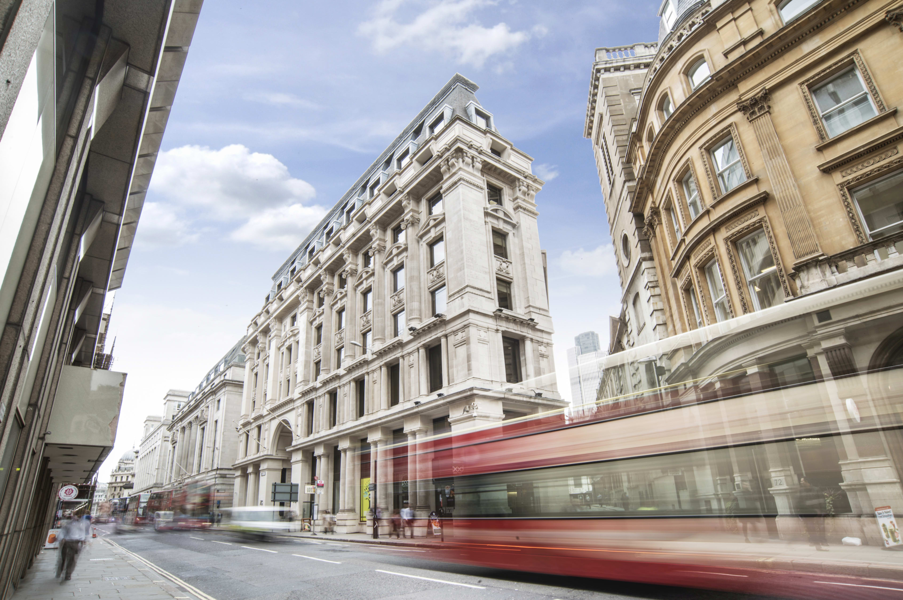The image shows a city street with historic buildings on either side and a blurred red bus moving through the scene.