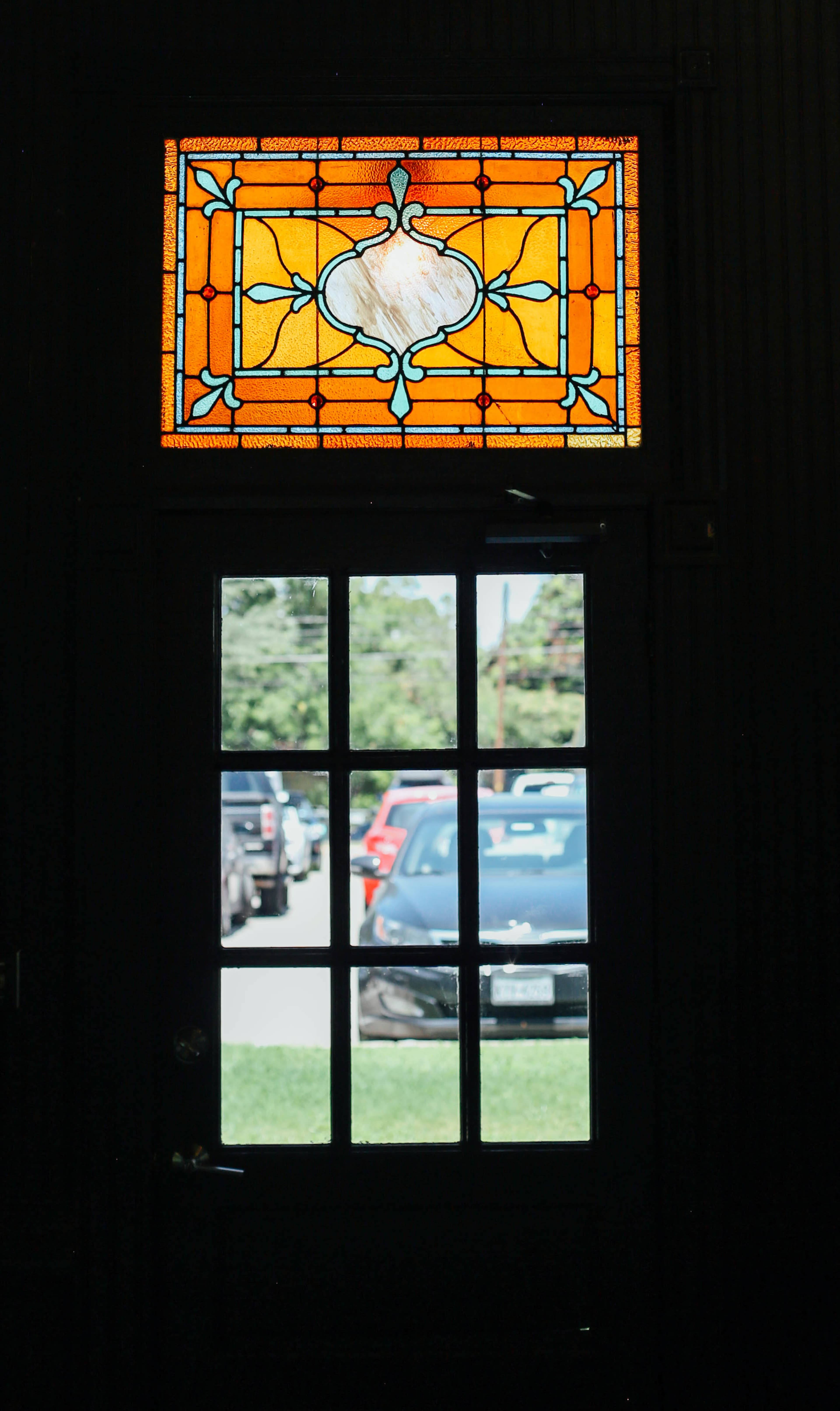 A decorative stained glass window above a door, with parked cars visible through the glass.