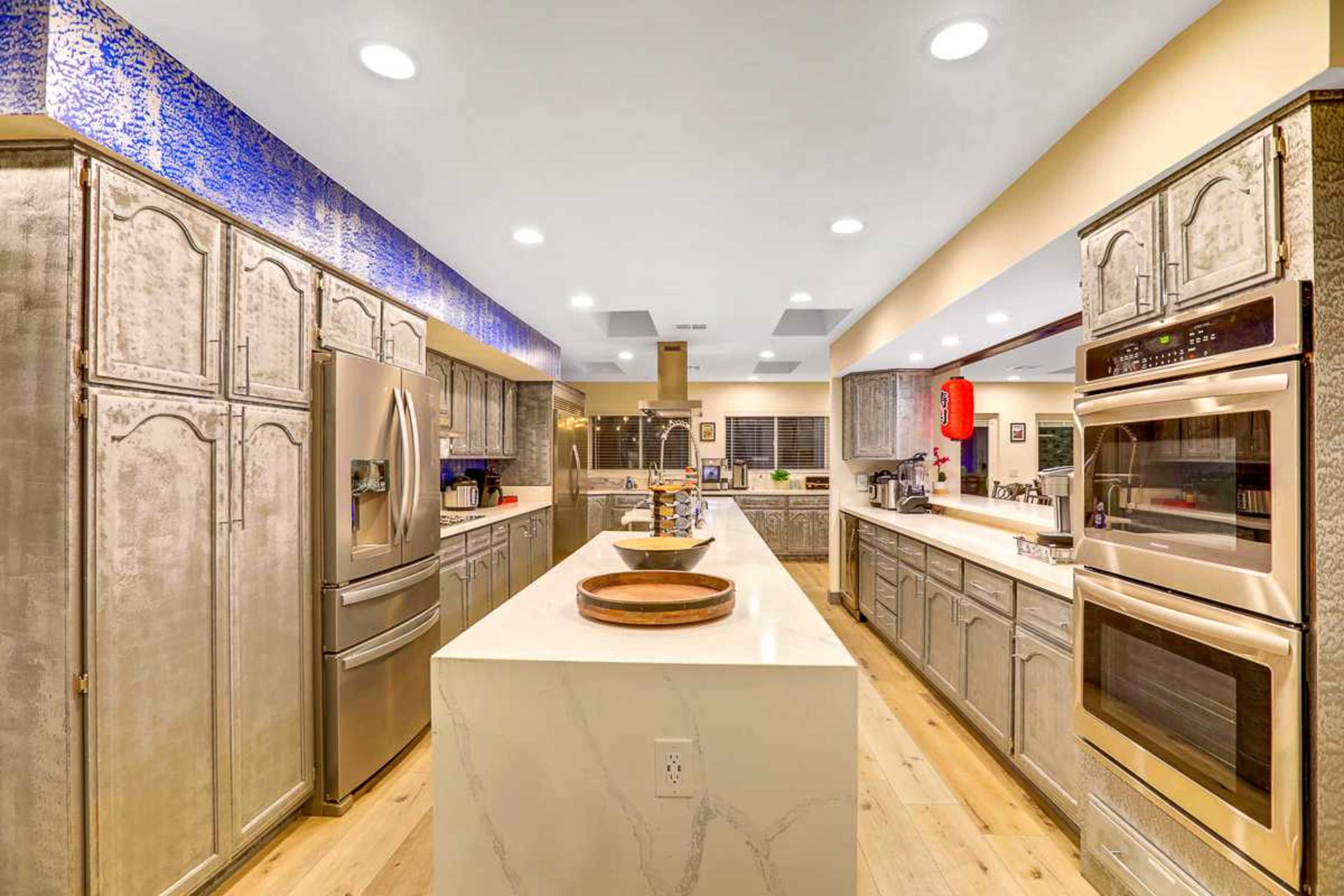 The kitchen features modern appliances and a central island with a light-colored countertop, surrounded by textured cabinetry and bright overhead lighting.