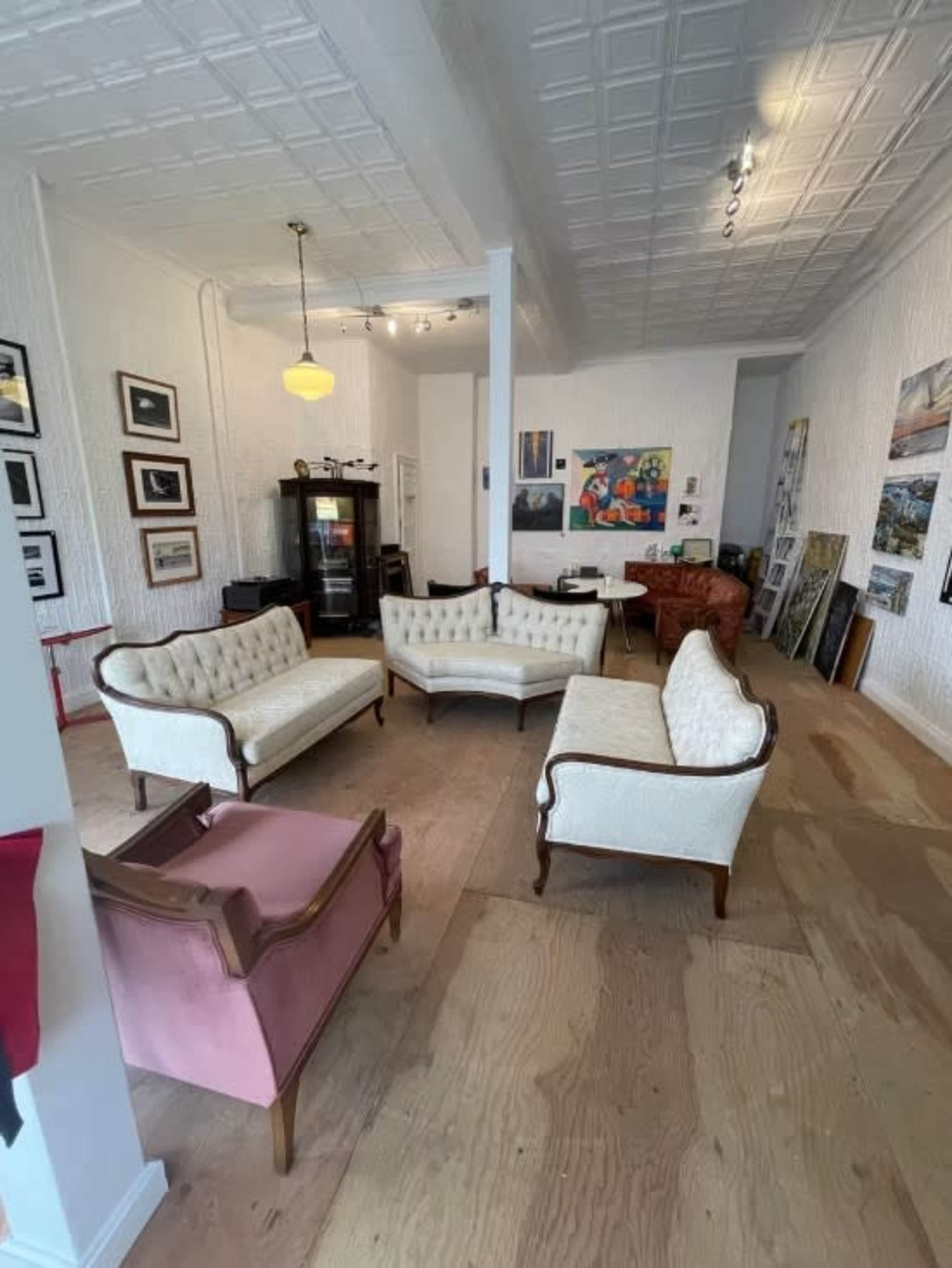 The image shows a spacious room with several seating areas featuring white upholstered couches and a pink chair, decorated with framed art on the walls.
