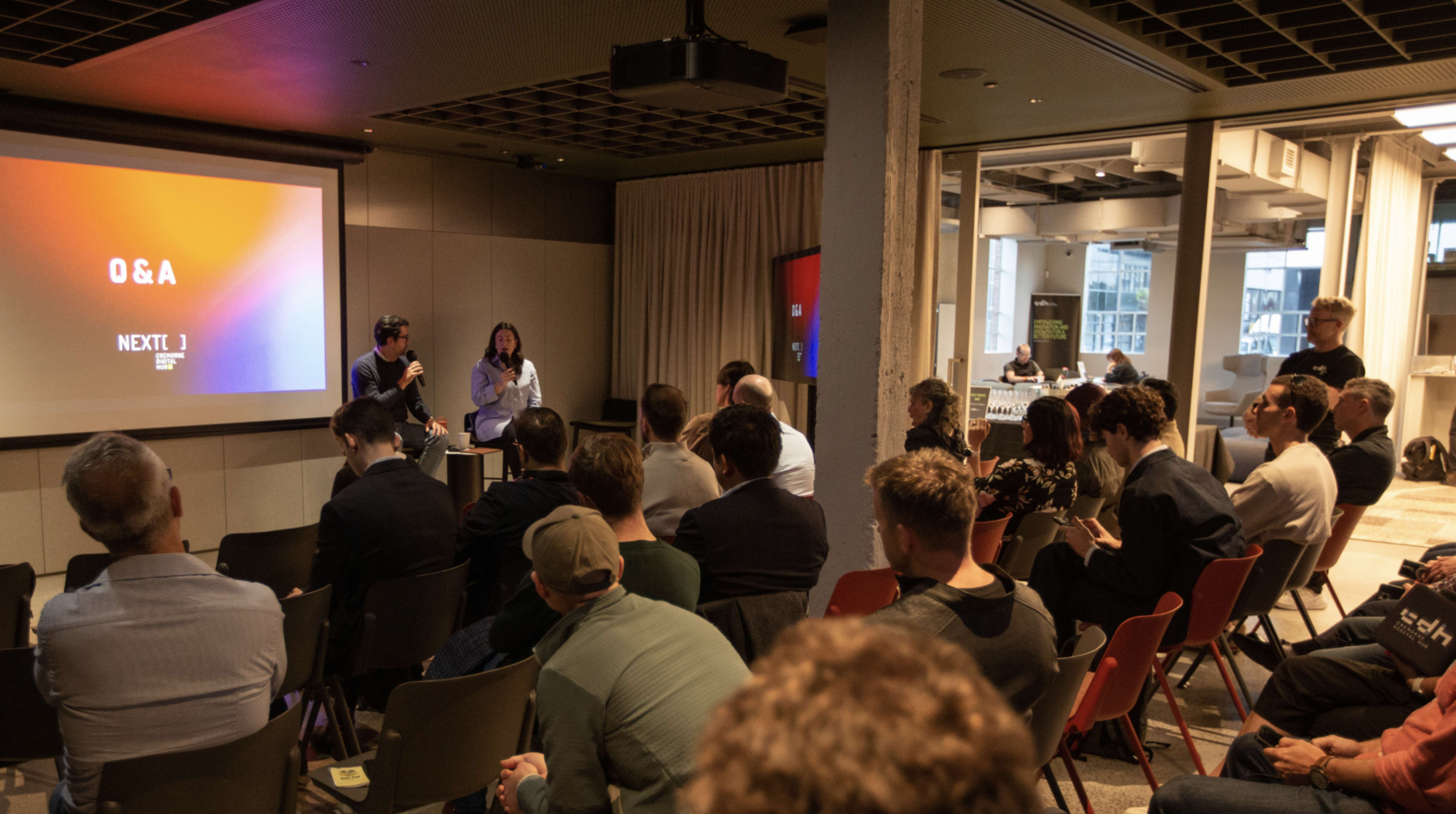 A panel discussion is taking place in a modern conference room, with attendees seated and focused on the speakers at the front.
