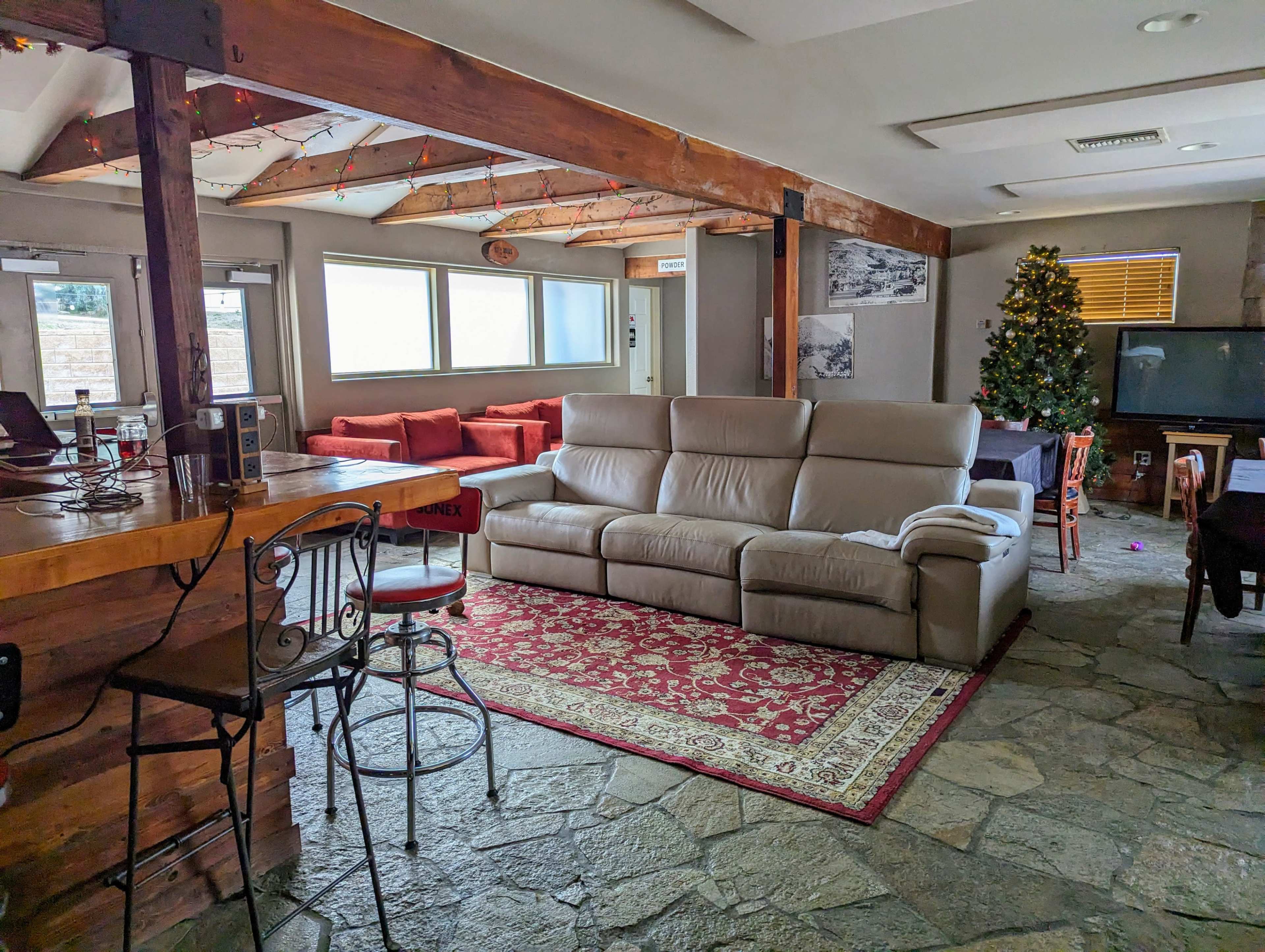 A spacious living area featuring a white leather couch, a red carpet, a Christmas tree, and wooden beams supporting the ceiling.