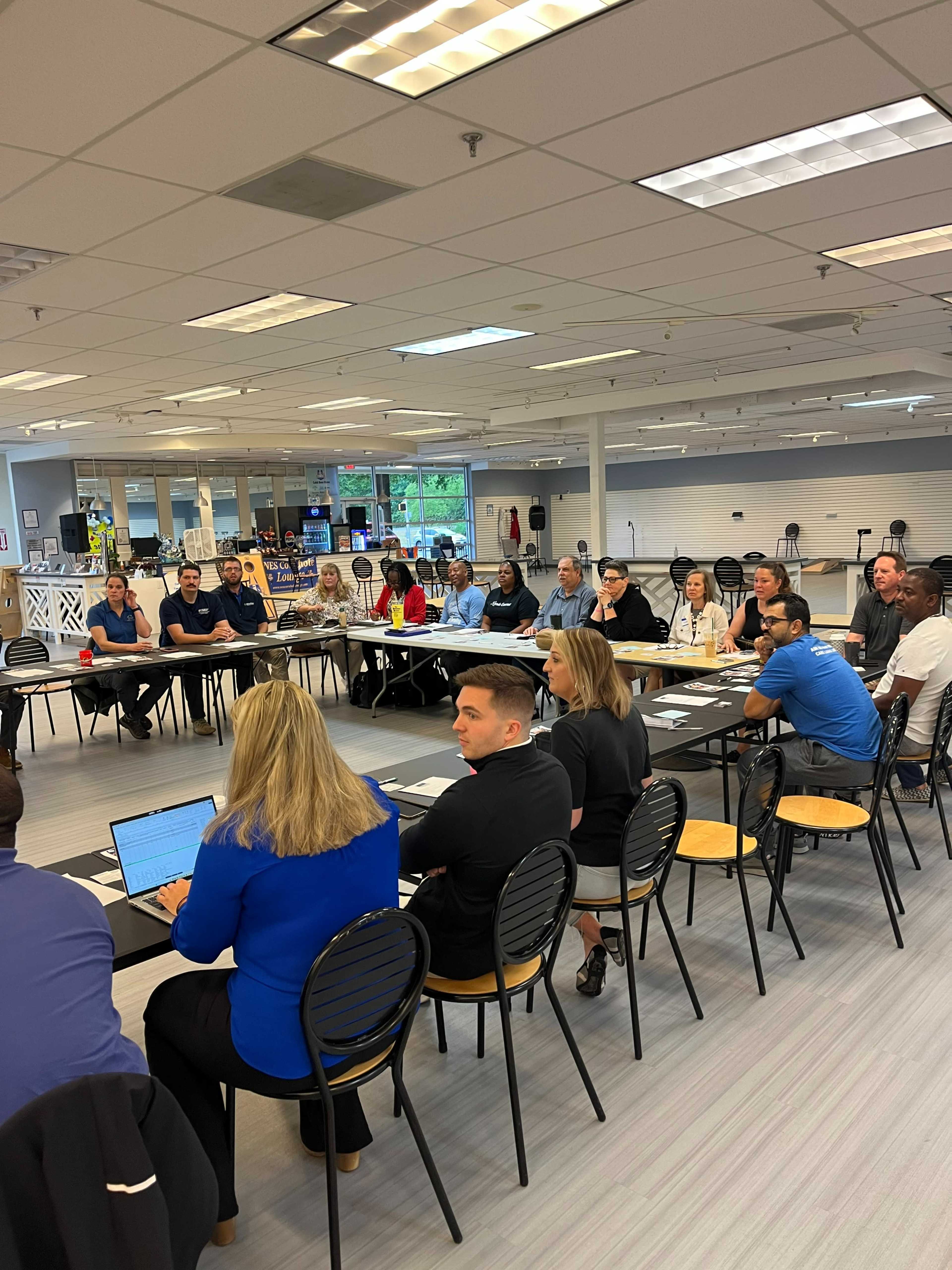 A group of professionals sits around a long table in a large, well-lit meeting room, engaging in discussion.