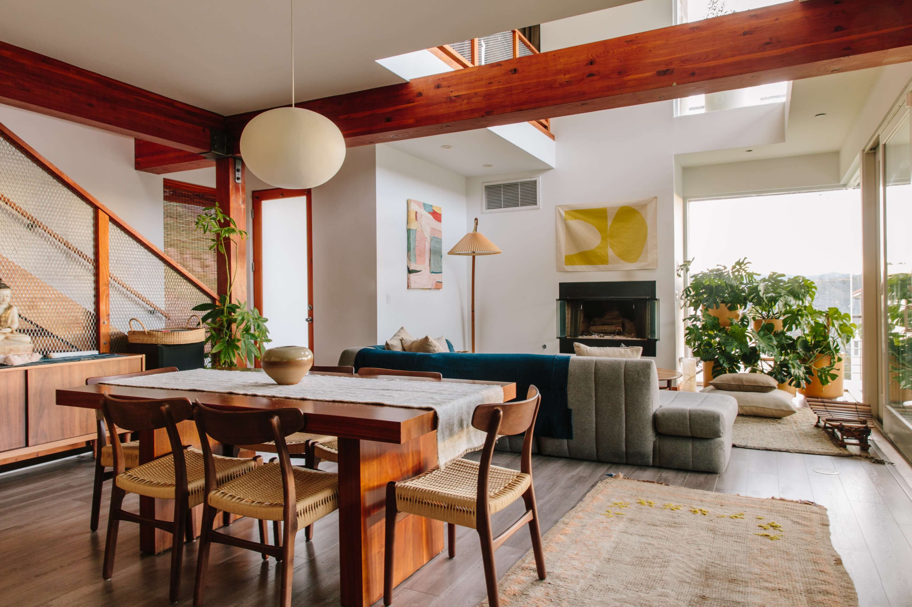 A modern living space with a wooden dining table, a sectional sofa, and large windows that allow natural light to enter.