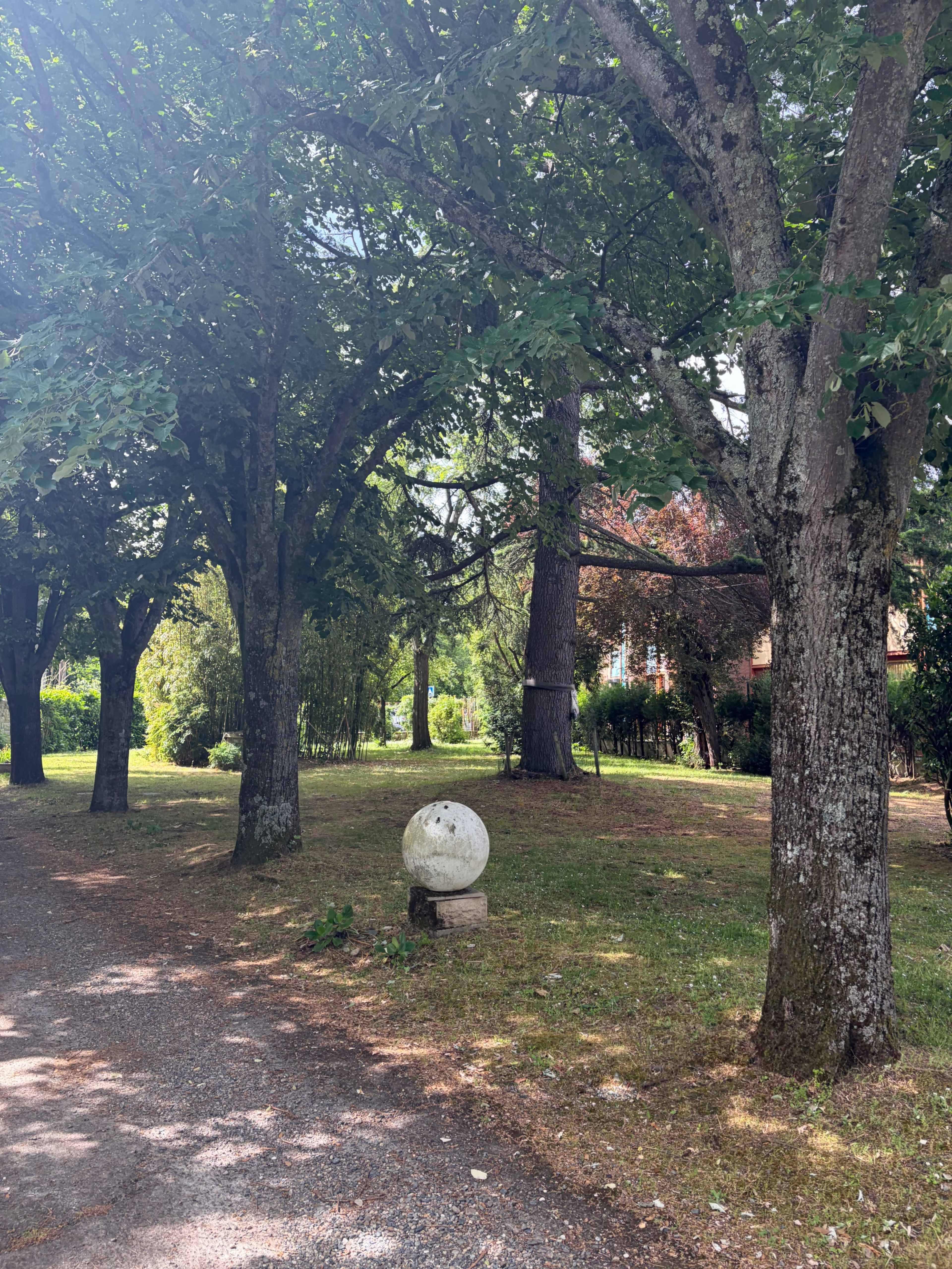 A stone sphere sits on a pedestal among trees in a park-like setting.