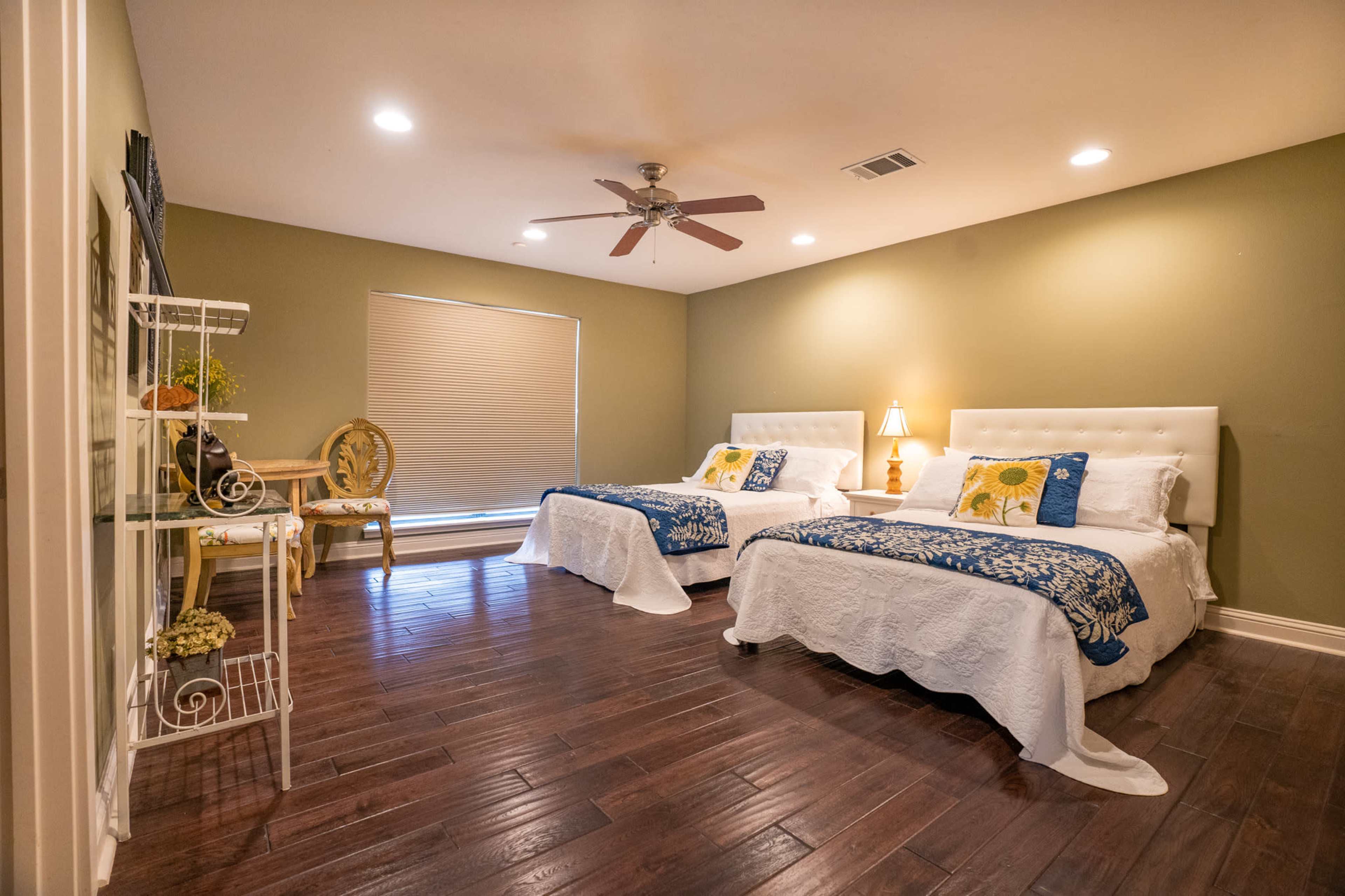 A spacious bedroom with two twin beds, a small table with a chair, and a window covered by a blind.