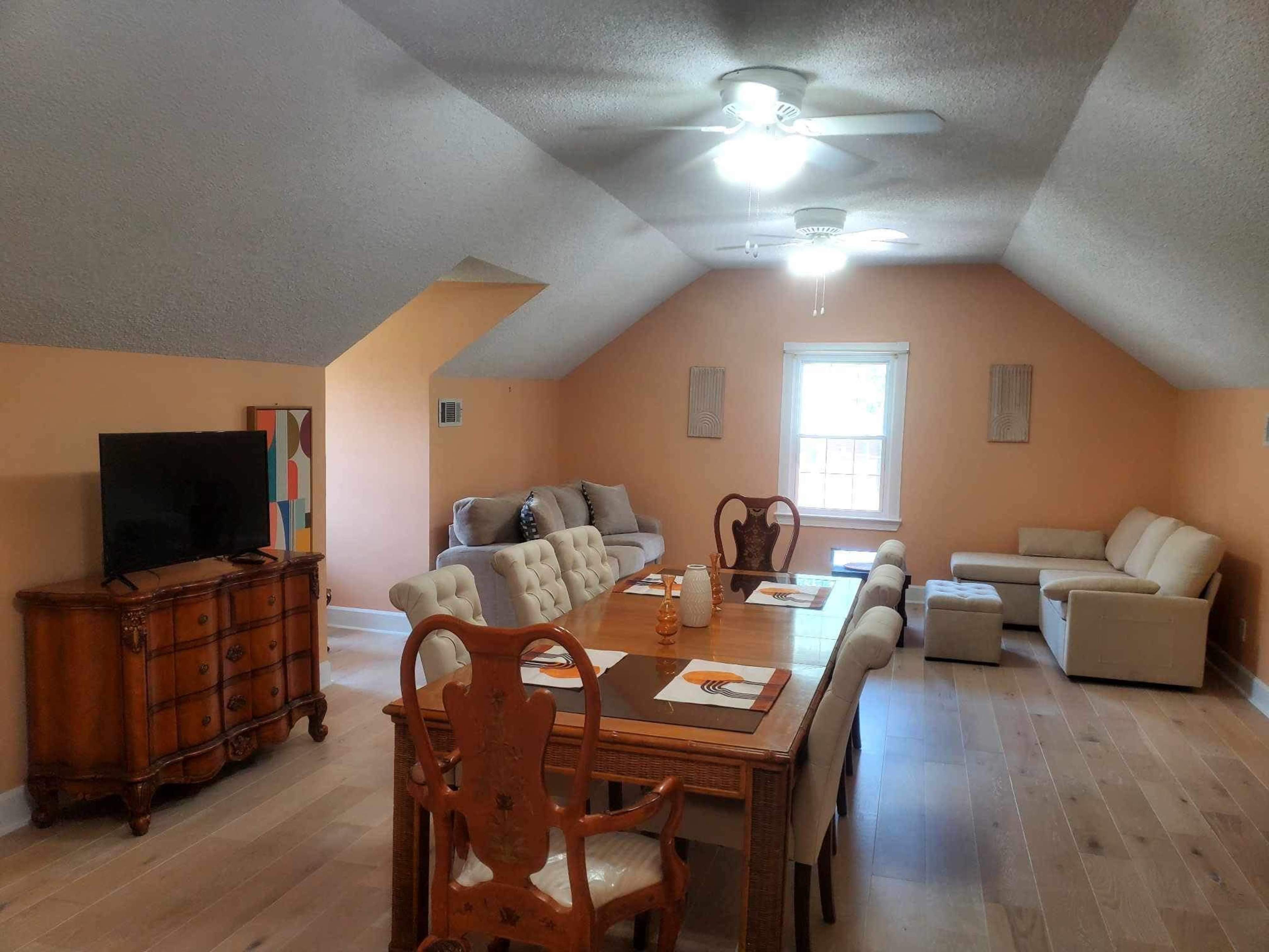 An attic living space furnished with a dining table, chairs, a television, and a seating area with a couch.