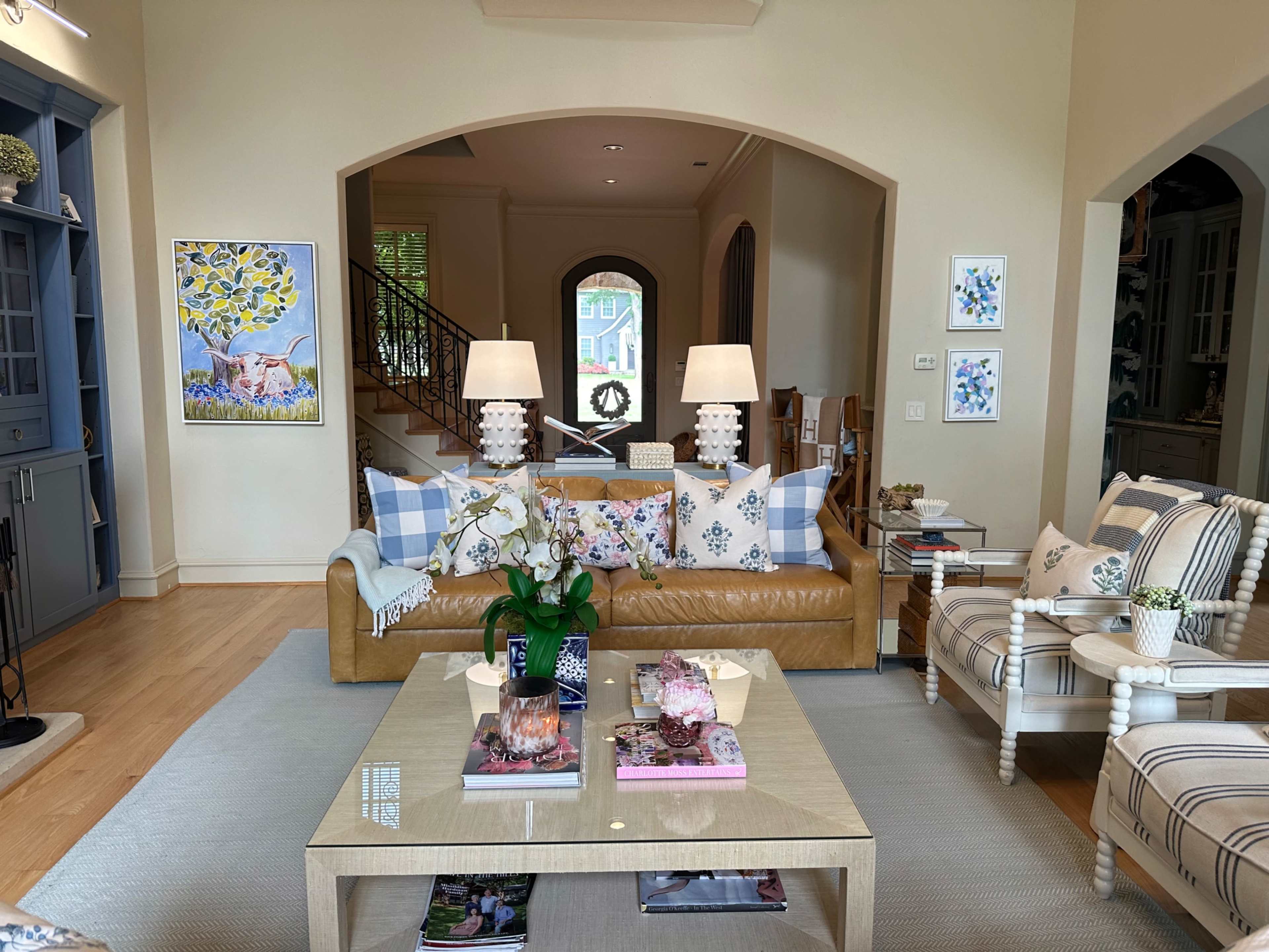 A spacious living room with a brown leather sofa adorned with decorative pillows, a coffee table in the center, and a staircase in the background.