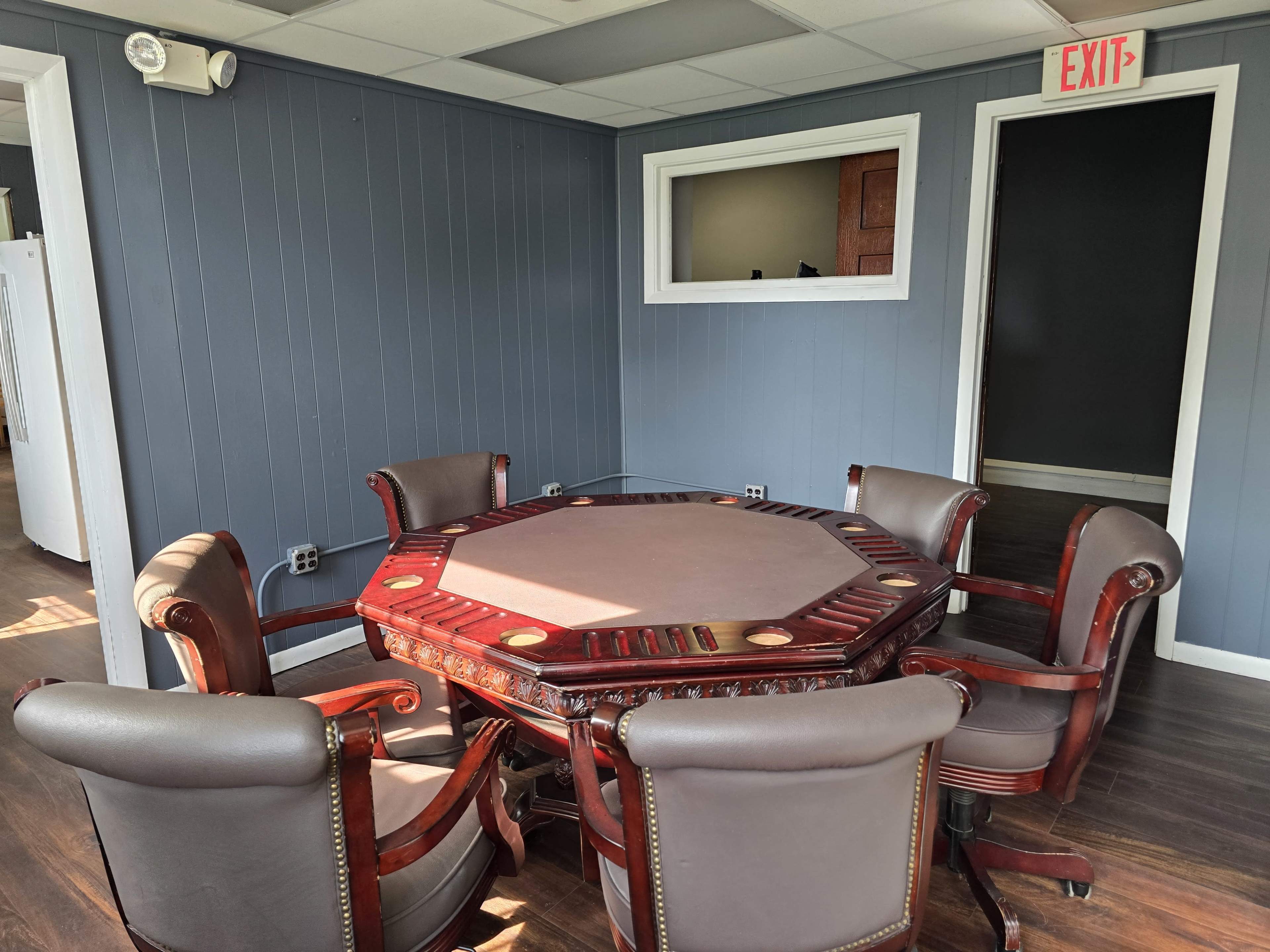 The image shows an octagonal wooden table surrounded by six upholstered chairs in a room with blue walls and a window.