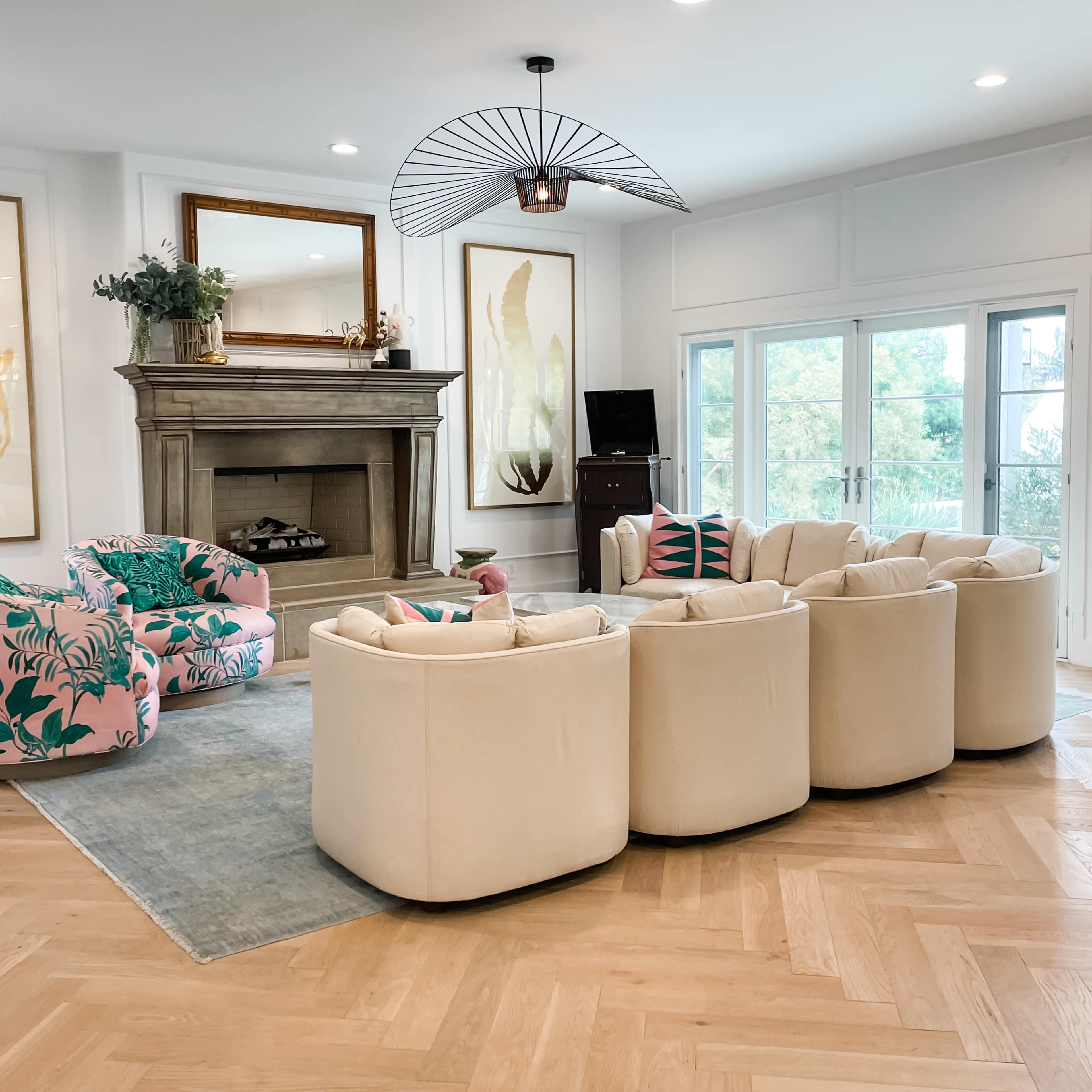 The living room features a circular arrangement of cream-colored chairs around a light blue rug, with a large fireplace and tropical-patterned armchairs in the background.