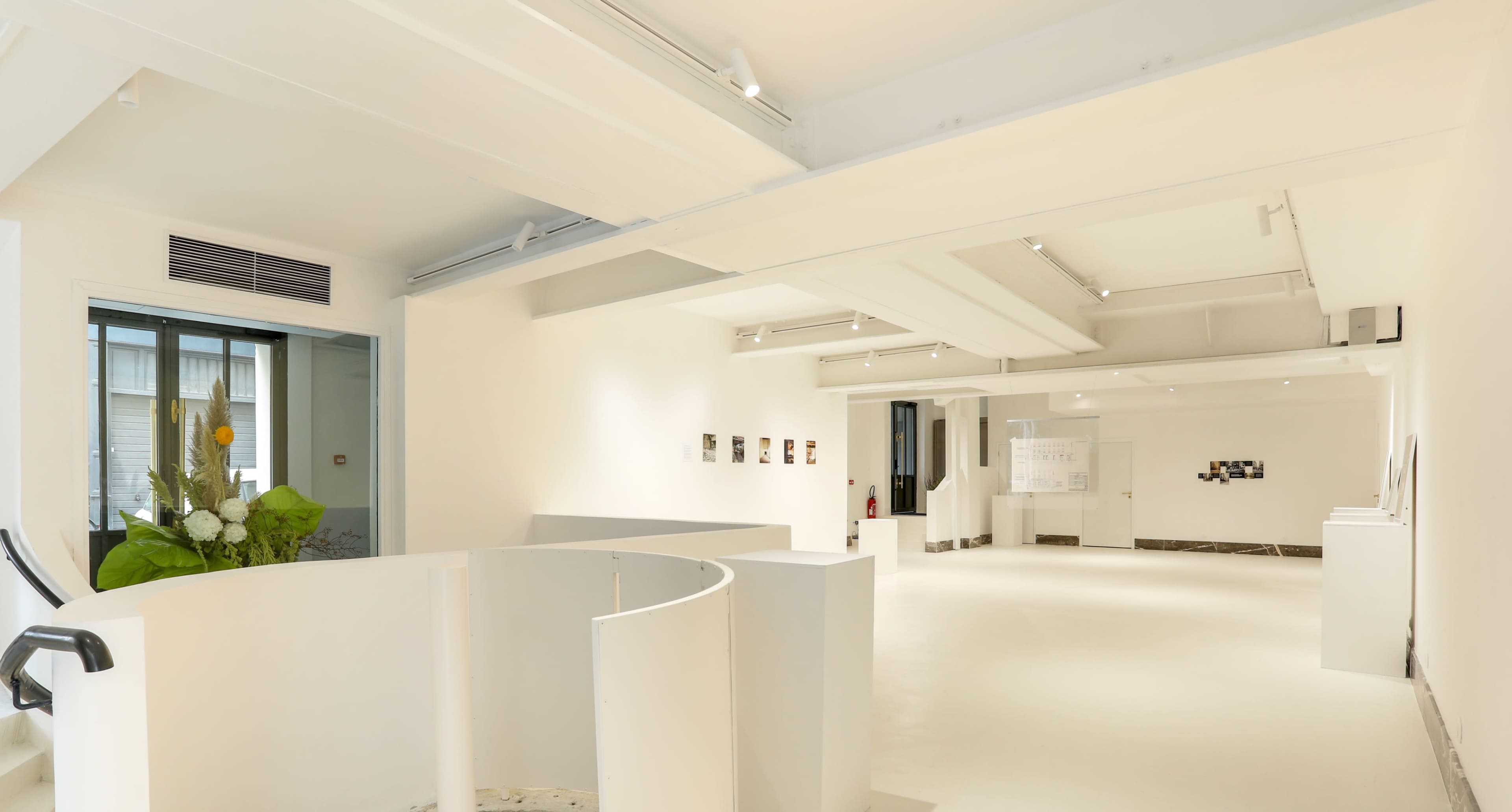 A spacious, modern art gallery with white walls and minimalistic decor, featuring artwork displayed on the walls and a curved structure in the foreground.