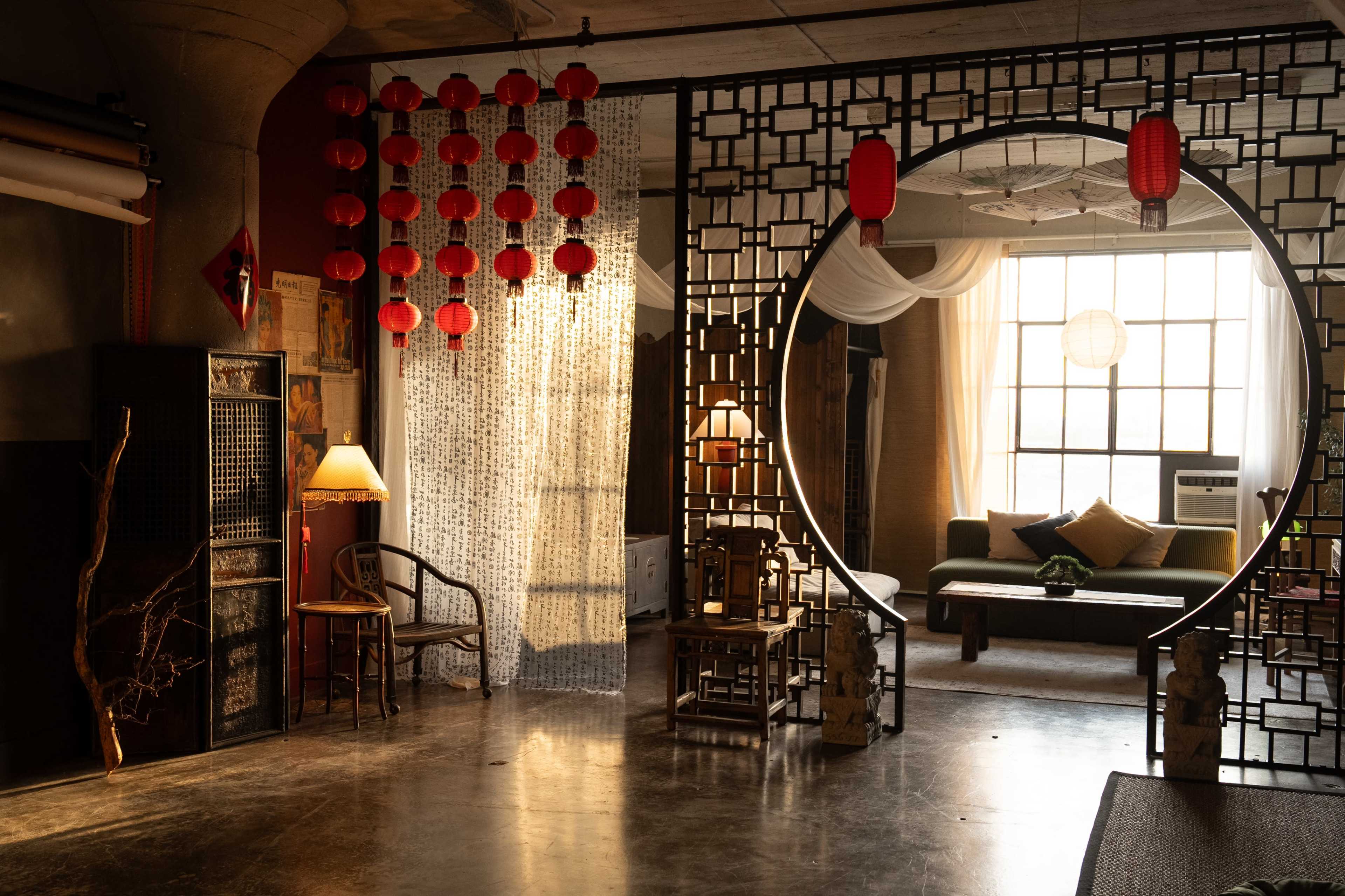 A spacious room with a circular entryway surrounded by decorative screens, traditional lanterns hanging from the ceiling, and various furniture arrangements including a sofa and a chair.