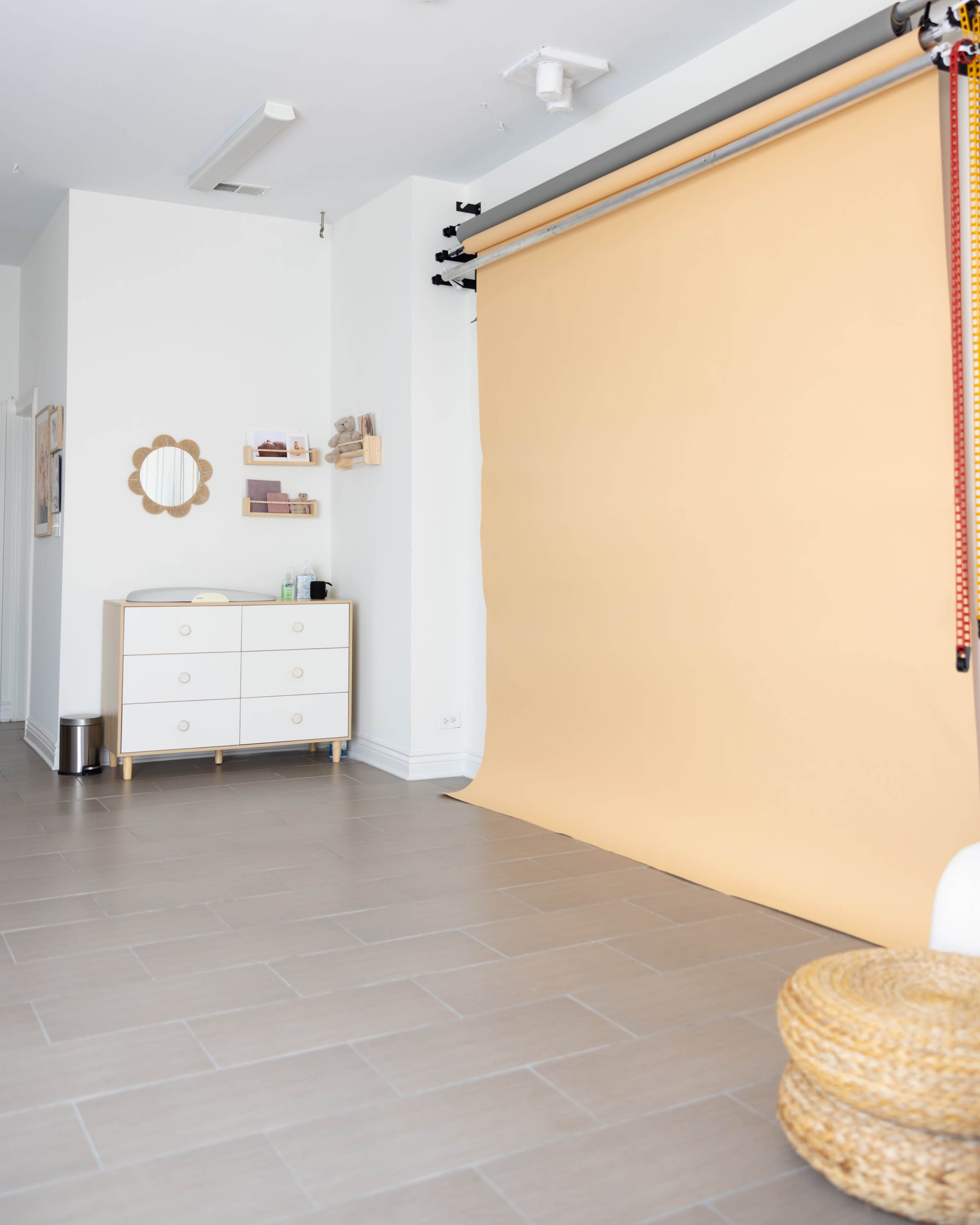 A spacious room features a plain peach backdrop, a low white dresser, and a round mirror mounted on the wall.