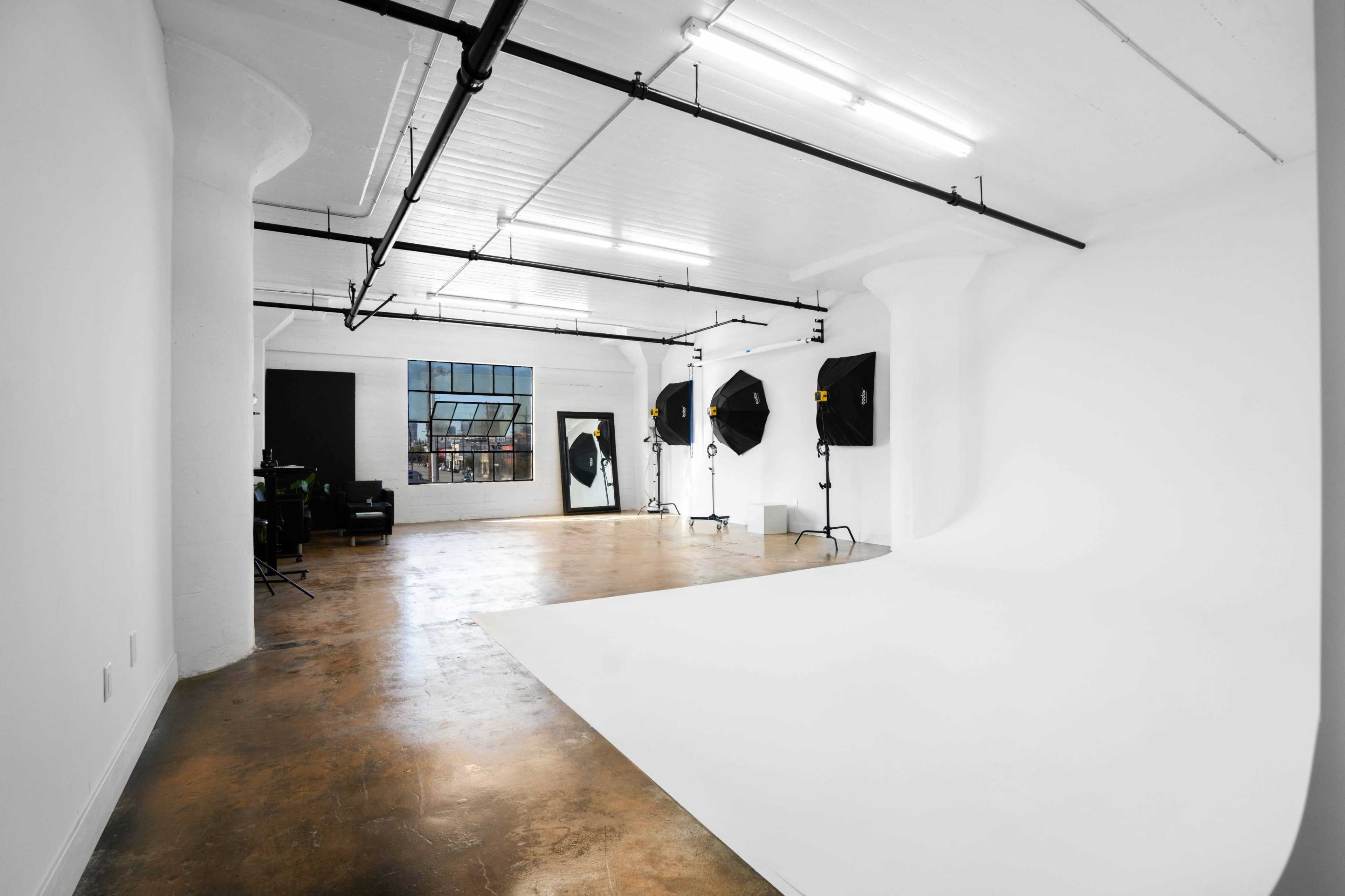 A spacious photography studio with a white backdrop and professional lighting equipment set up around the area.