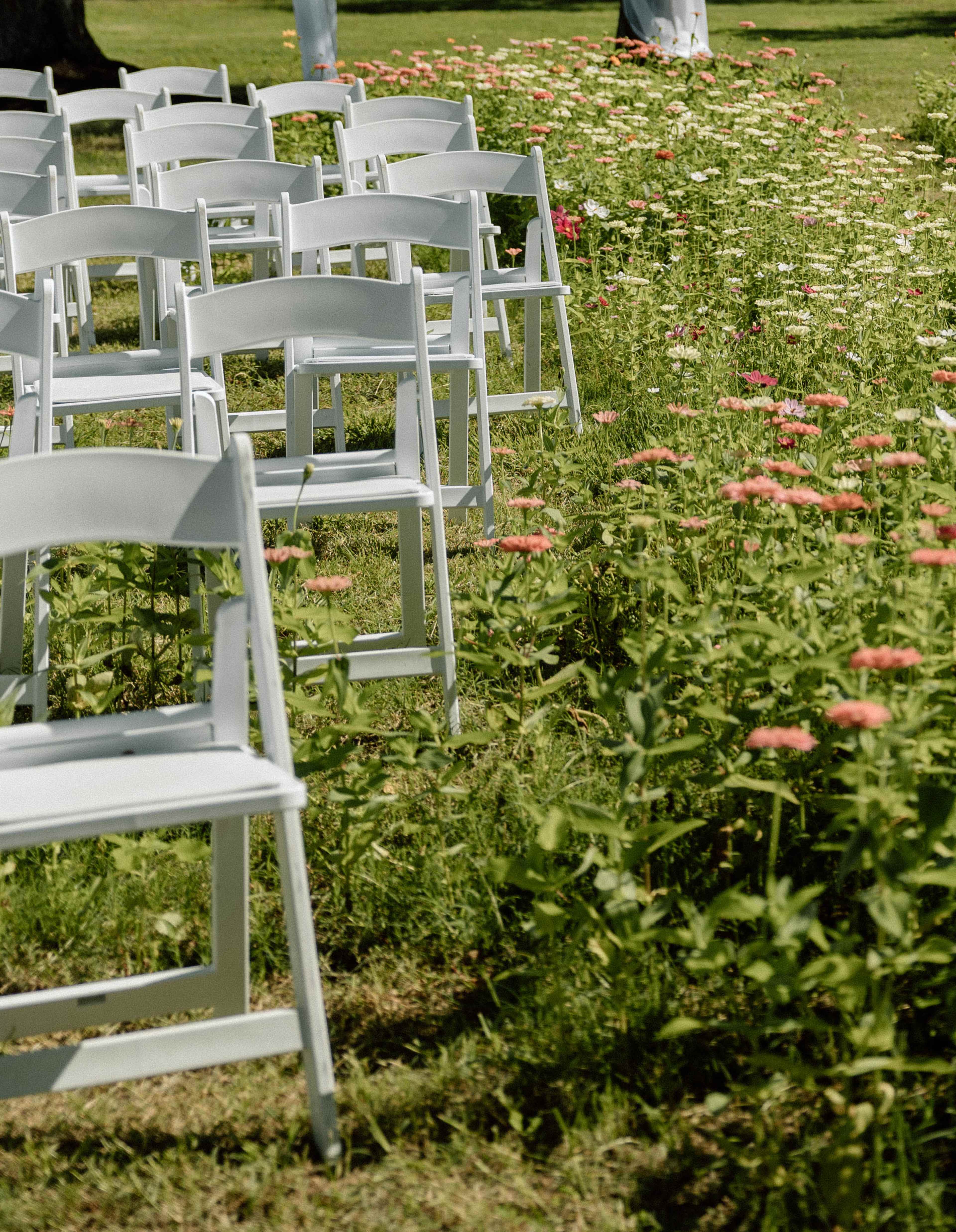 White chairs are arranged in a grassy area surrounded by blooming flowers.