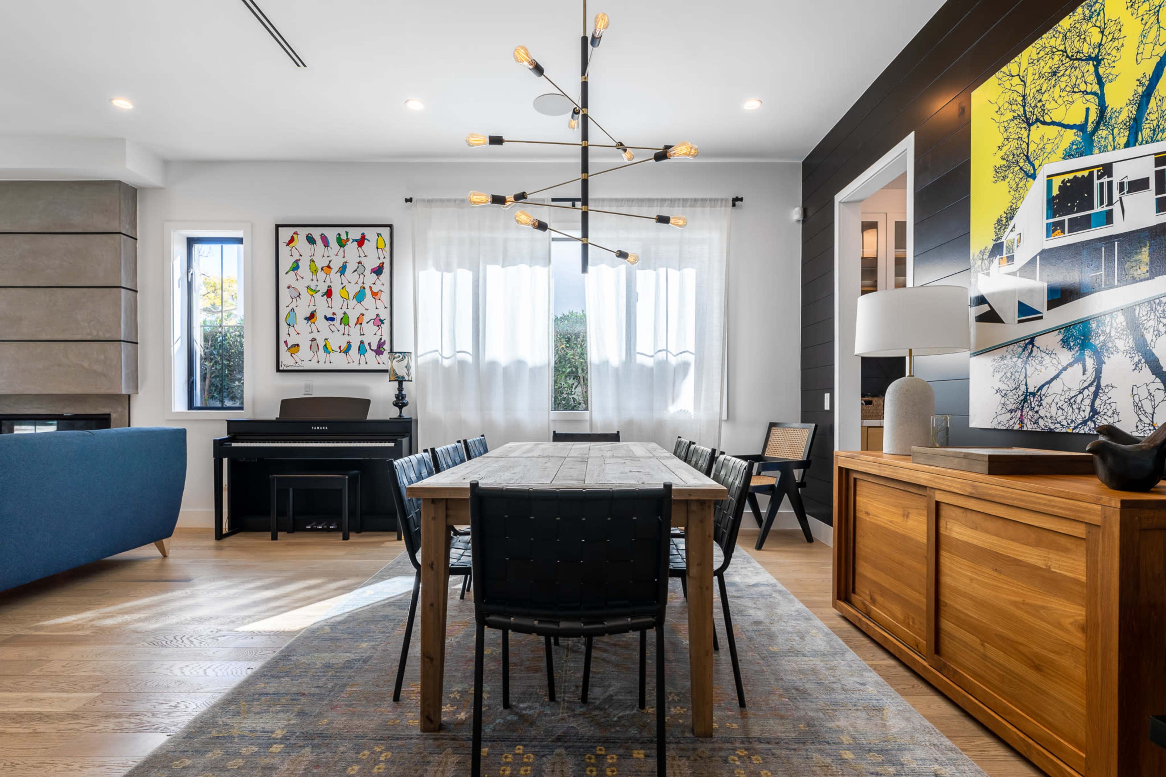 A modern dining room featuring a wooden table surrounded by black chairs, a piano in the corner, and colorful artwork on the walls.