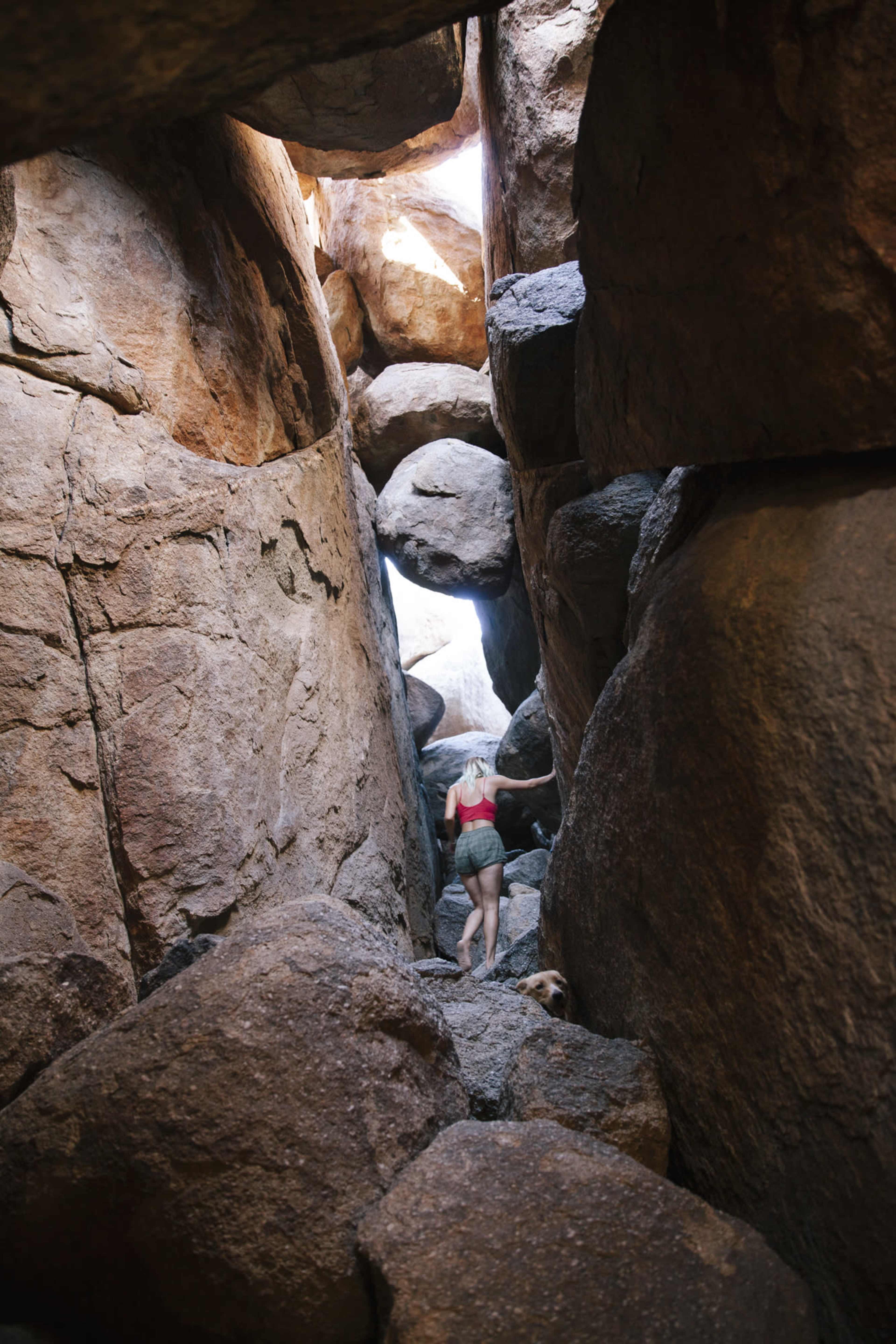 A person navigates through a narrow passage formed by large boulders within a rocky canyon.