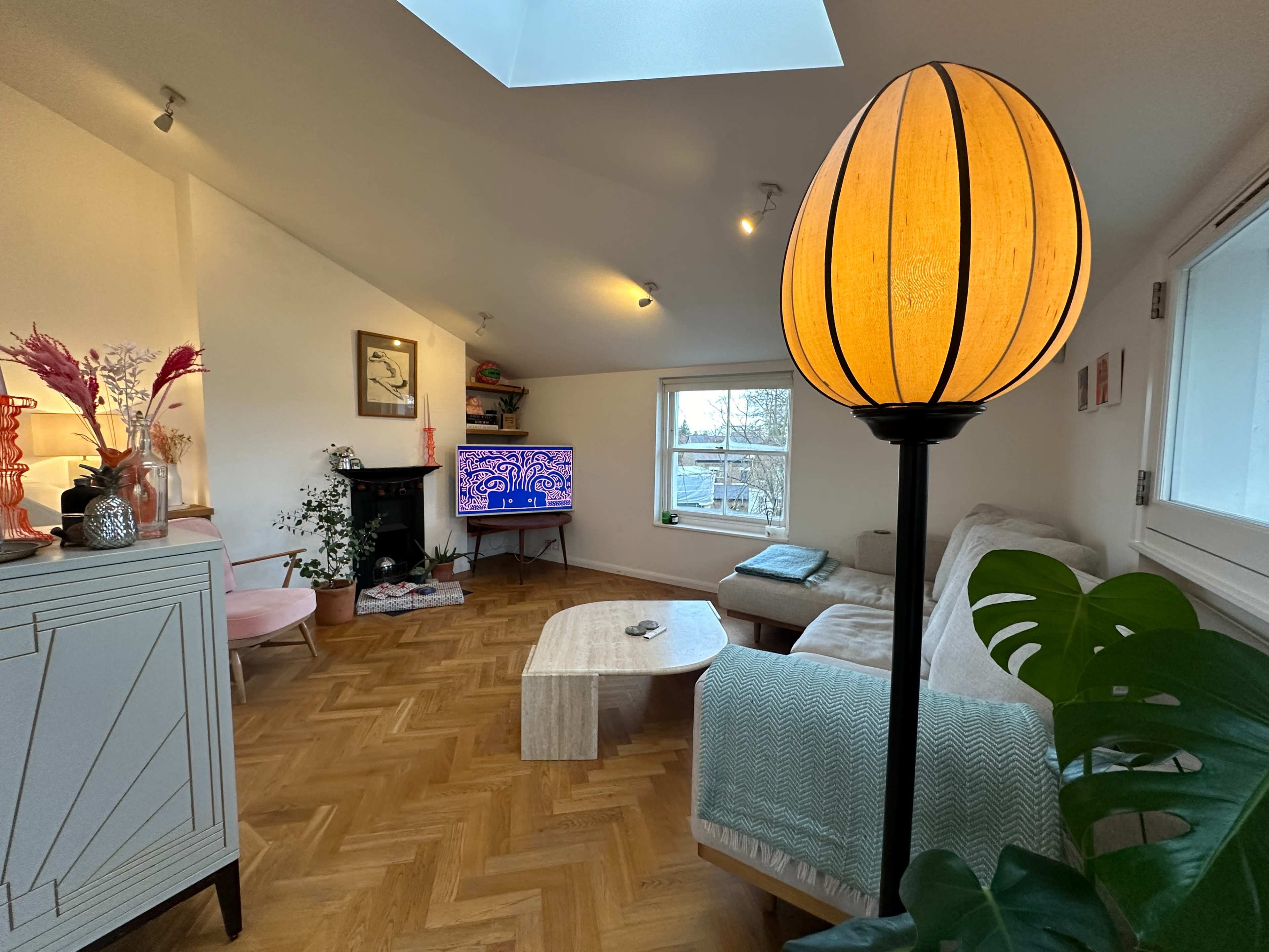 The living room features a light-colored sofa, a wooden coffee table, a television on the wall, and a tall lamp with an orange shade.