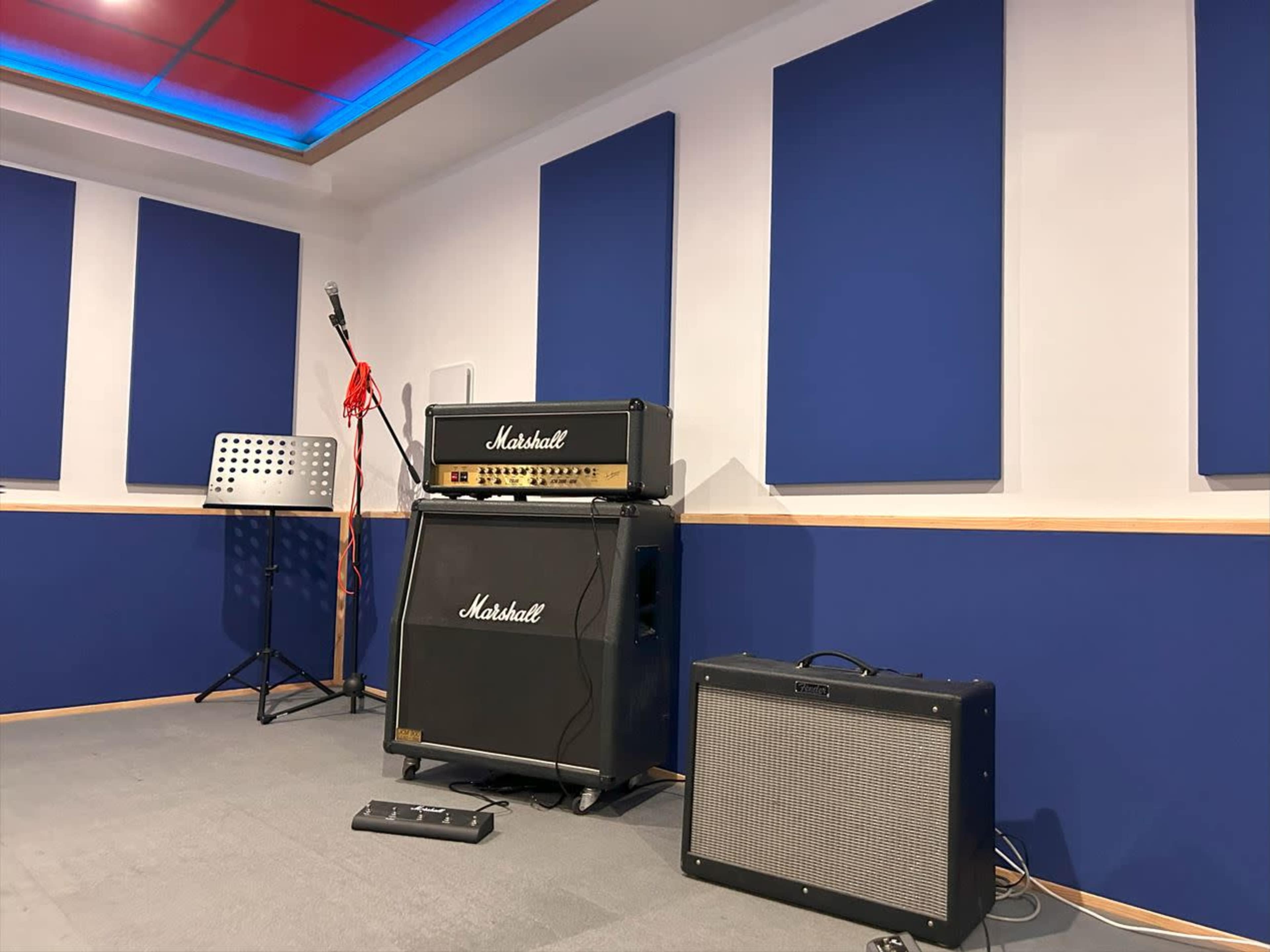 A music rehearsal studio with a Marshall amplifier stack, a microphone stand, and sound-absorbing panels on the walls.